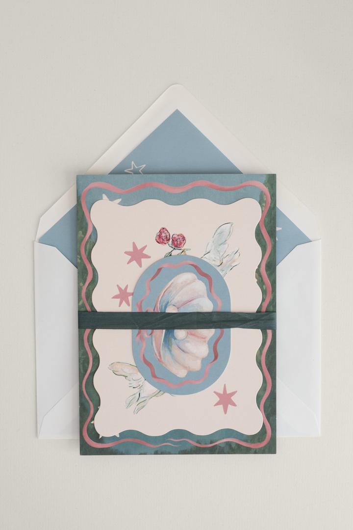 Coquette wedding invitation suite neatly stacked and finished with a dark green silk ribbon band, resting on top of an open, patterned envelope liner.
