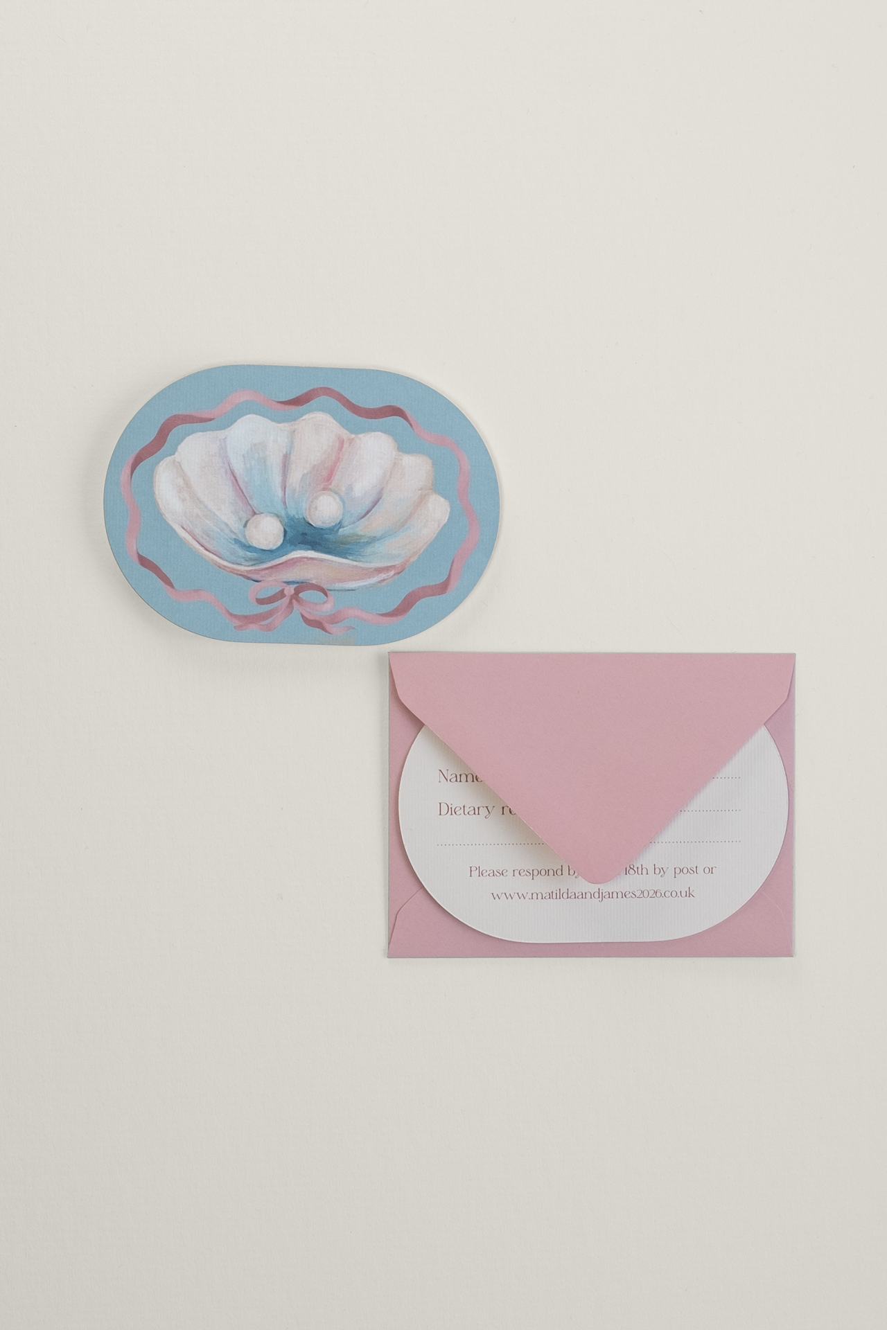 Coquette wedding RSVP card front showing a hand-painted shell illustration next to a soft pink return envelope, with the response side tucked inside the envelope flap.