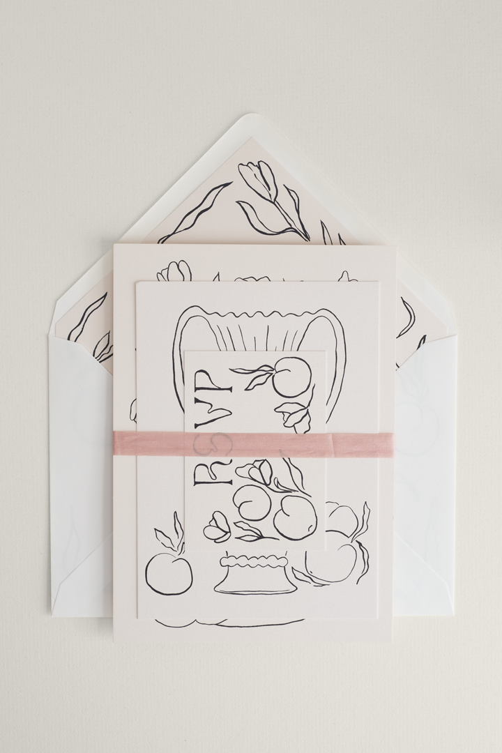 Artistic Tulips wedding invitation suite stacked and finished with a blush pink silk ribbon band, layered on top of a minimalist, ink-illustrated envelope liner.
