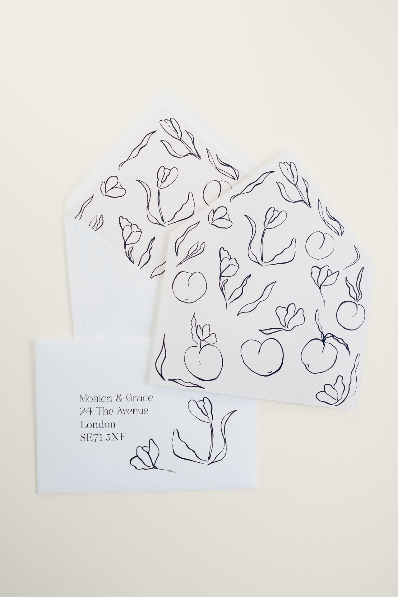 Flat lay of Tulips wedding envelopes and liners in black and white, displaying an envelope stuffed with the liner, the full floral illustration flat, and an addressed envelope.