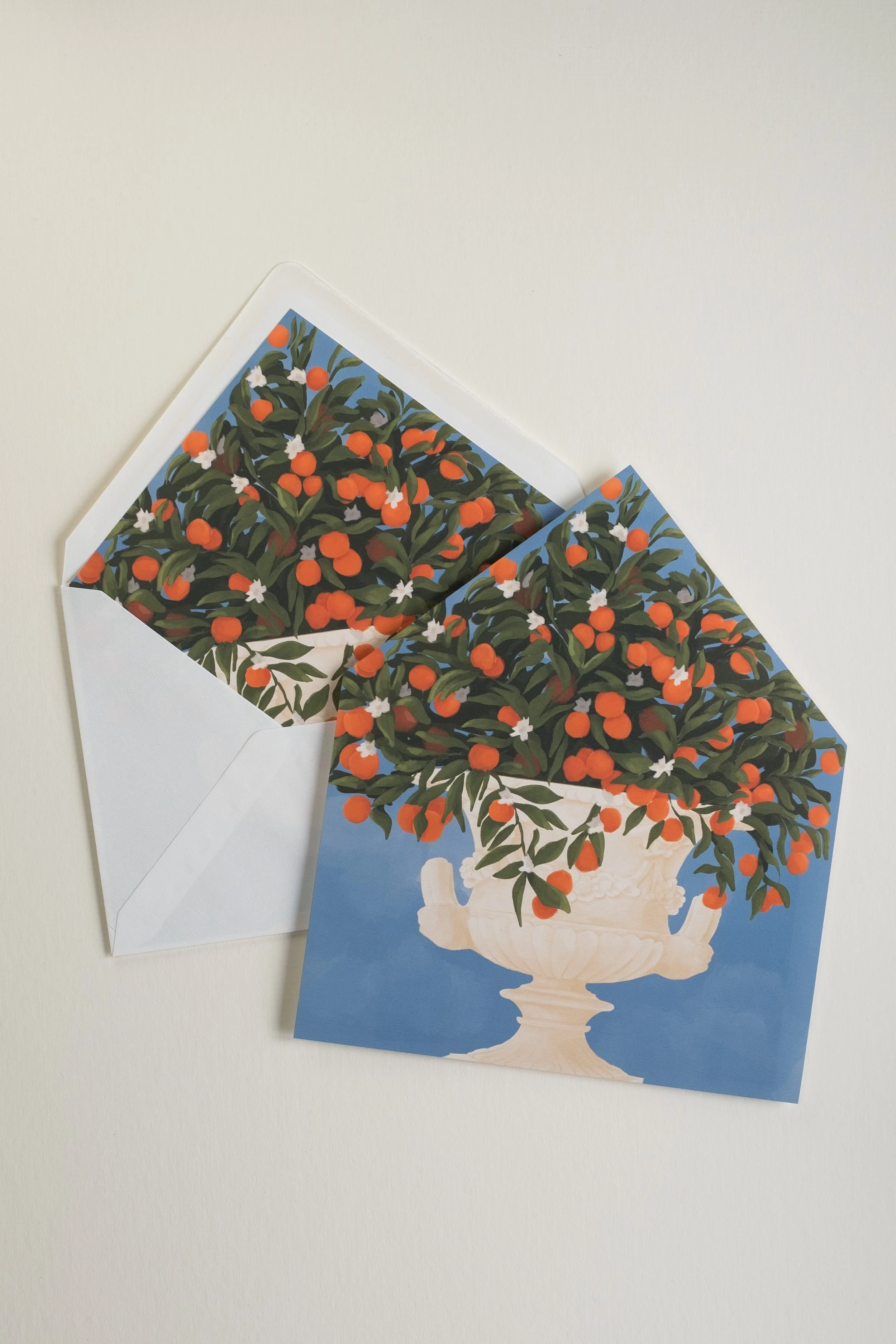 Flat Orangery wedding invitation liner featuring a classical urn overflowing with oranges, styled over an open envelope revealing the vibrant citrus pattern.