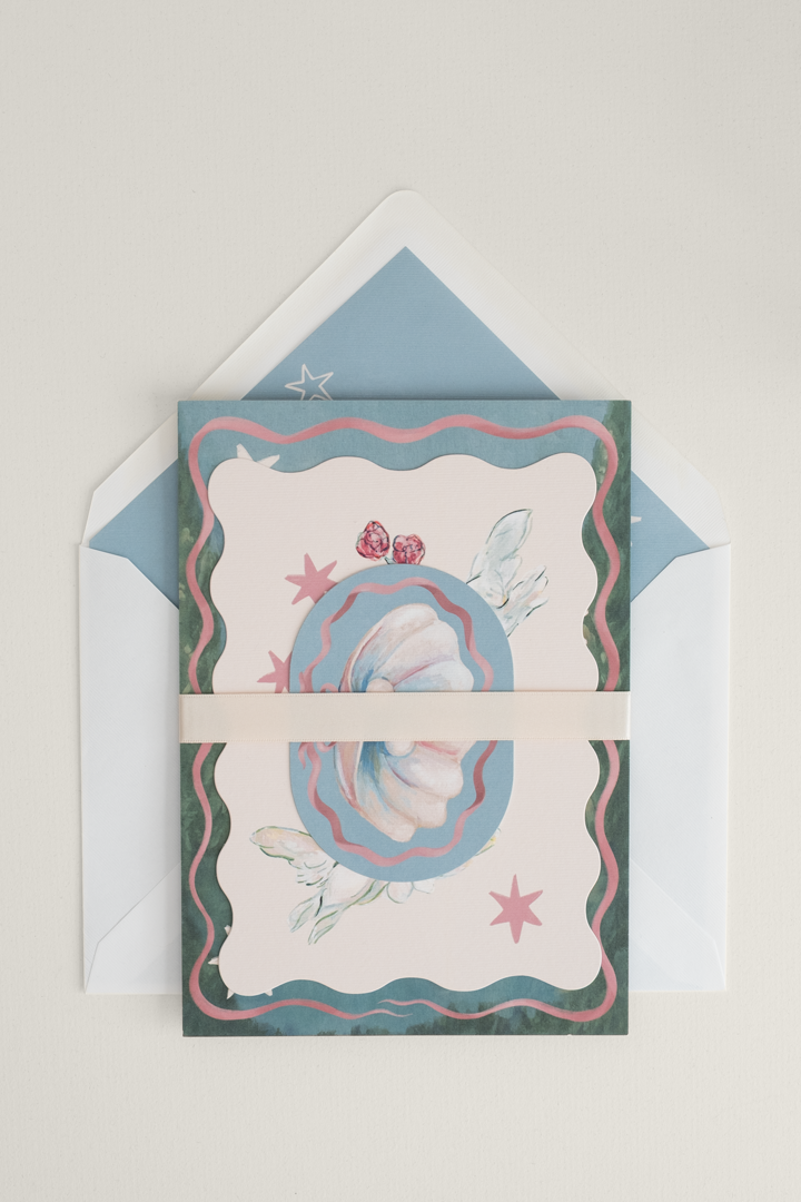 Coquette wedding invitation suite beautifully stacked and finished with a pearl satin ribbon band, displayed on top of an open, lined envelope.