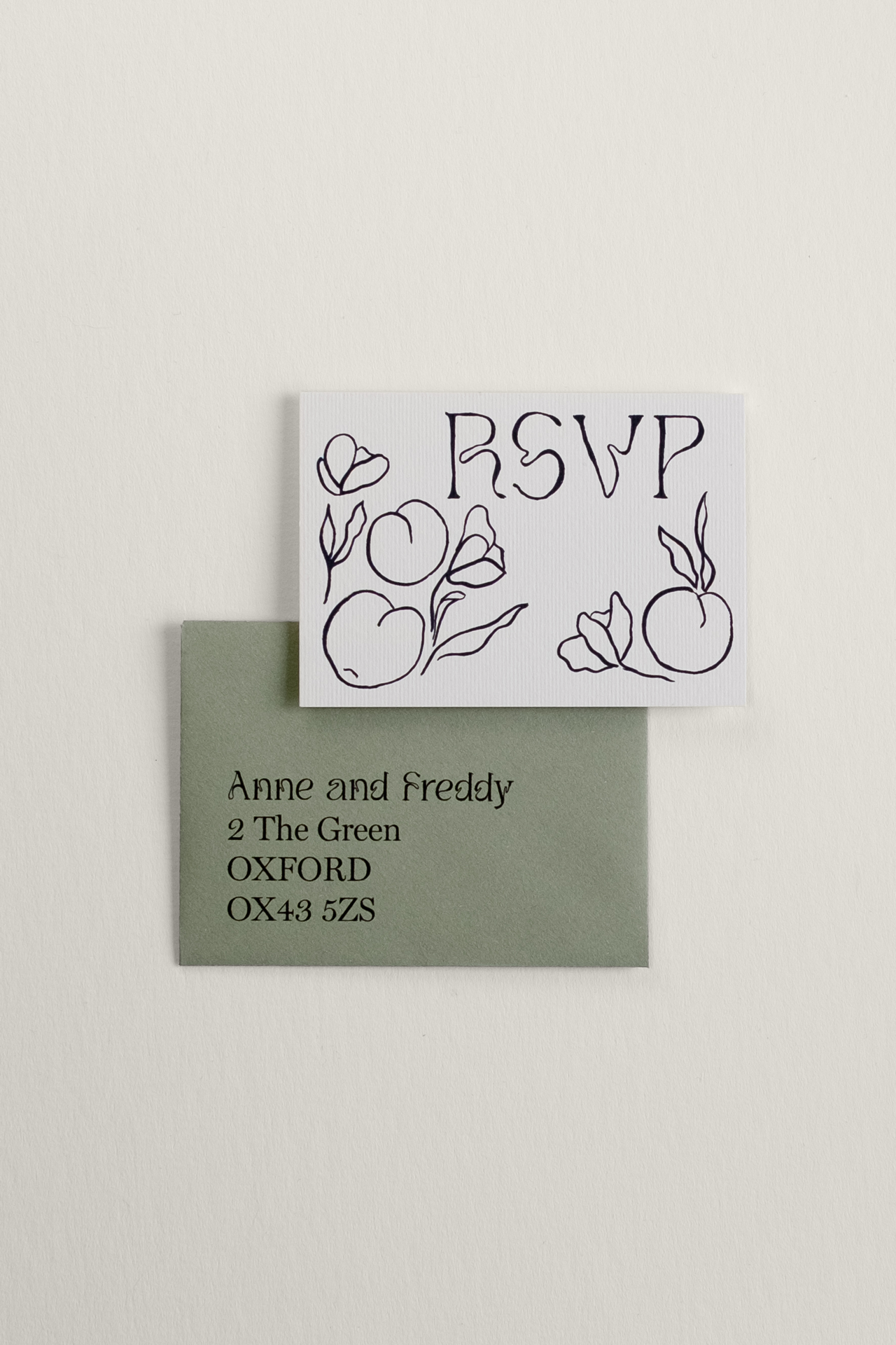 The front of the minimalist Tulips wedding RSVP card, featuring a bold black ink illustration of scattered tulips and fruit, displayed next to a sage green return envelope.