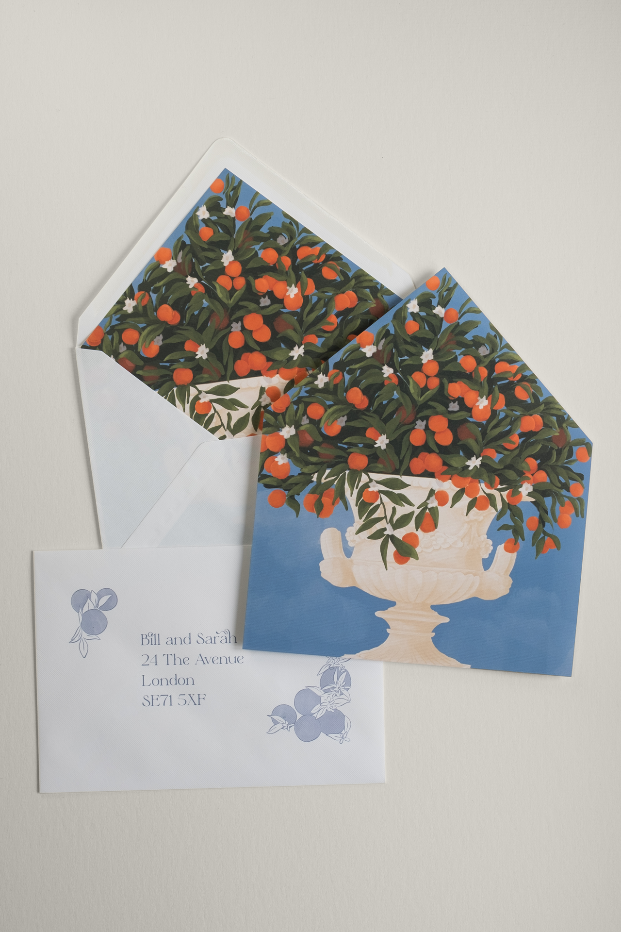 Flat lay of Orangery wedding envelopes and liners in sky blue and citrus orange, displaying an envelope stuffed with the liner, the full classical urn illustration, and an addressed envelope.