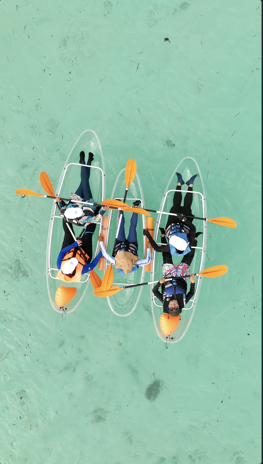 Three people in kayaks on calm water, paddling together, all wearing life jackets and sun hats.