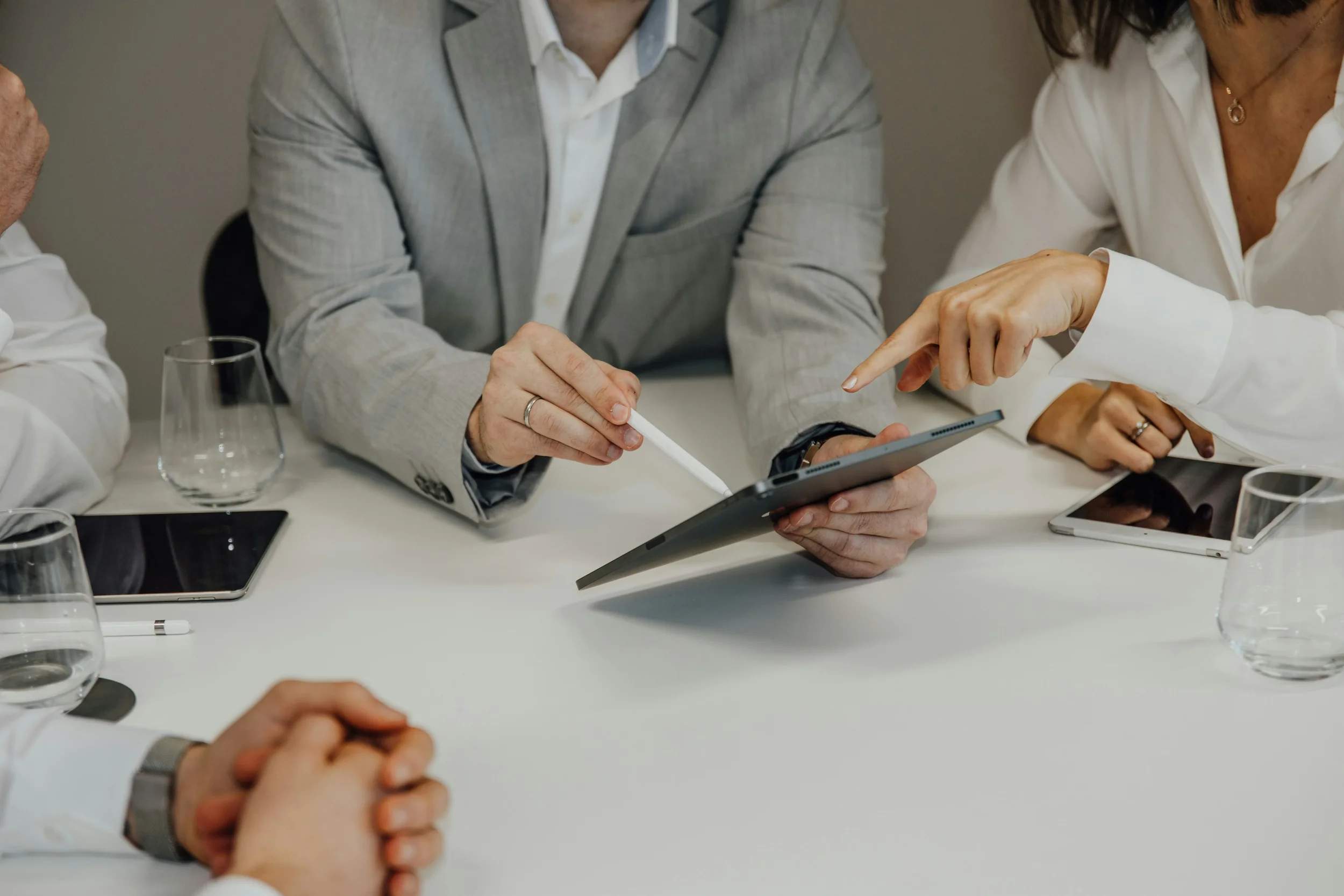 Two people at a meeting table with a laptop, notebook, and smartphone, engaging in discussion.