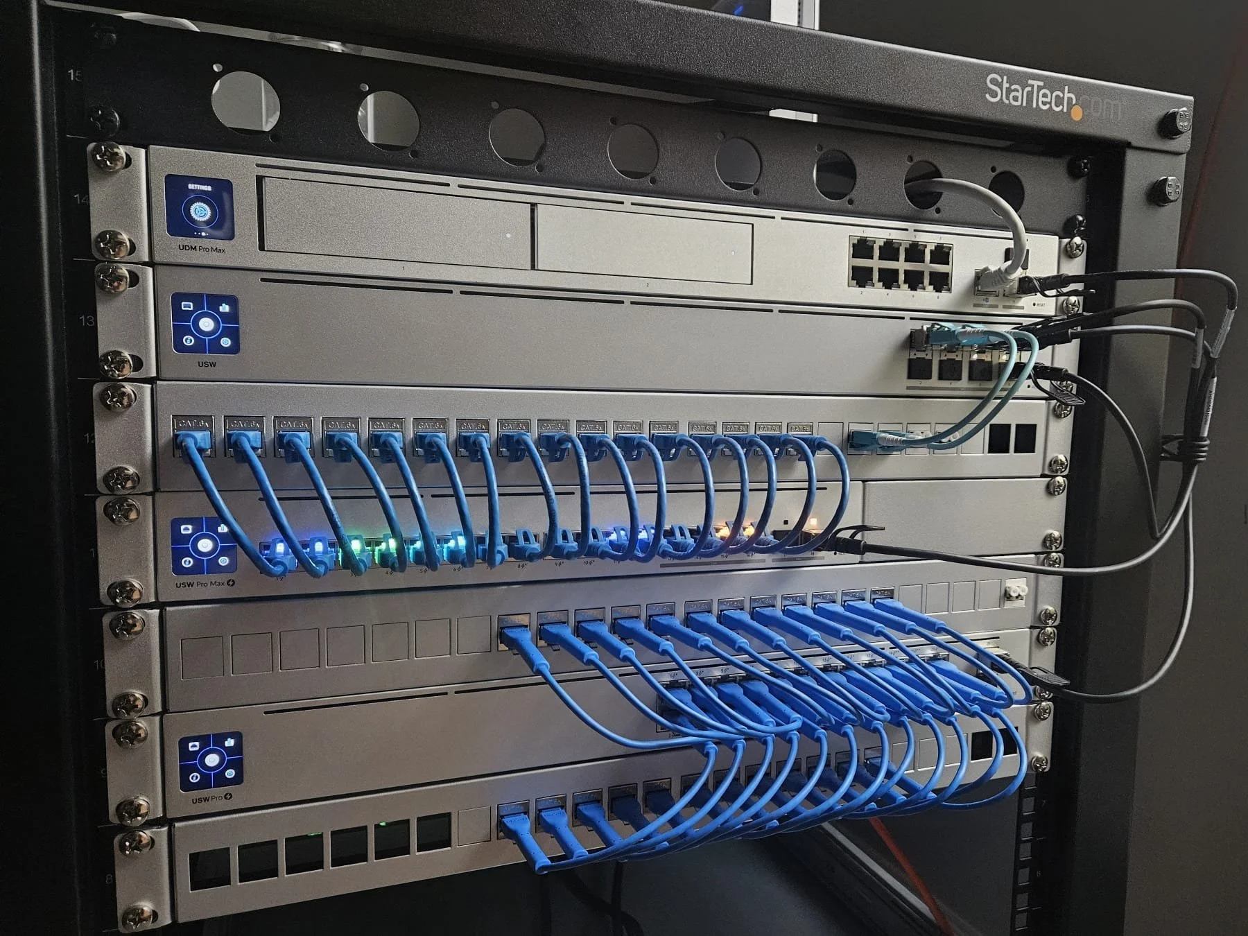A server rack with various network switches and patch panels connected by numerous blue Ethernet cables.