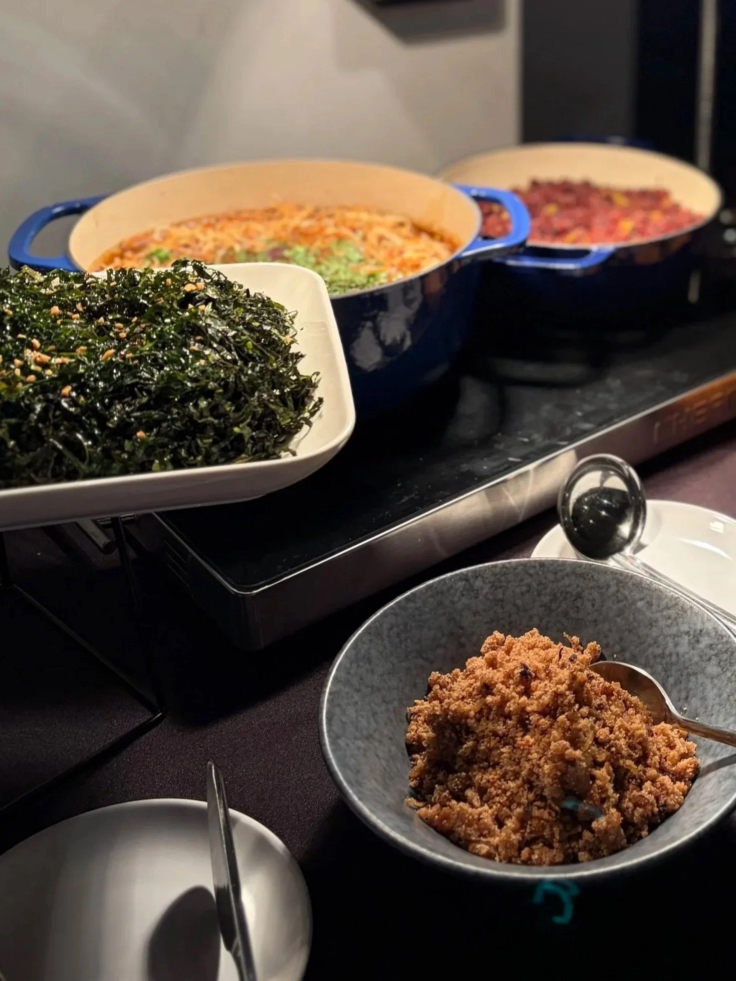 Asian buffet with three large dishes of food, a bowl of seaweed salad, and a bowl of seasoned ground meat.