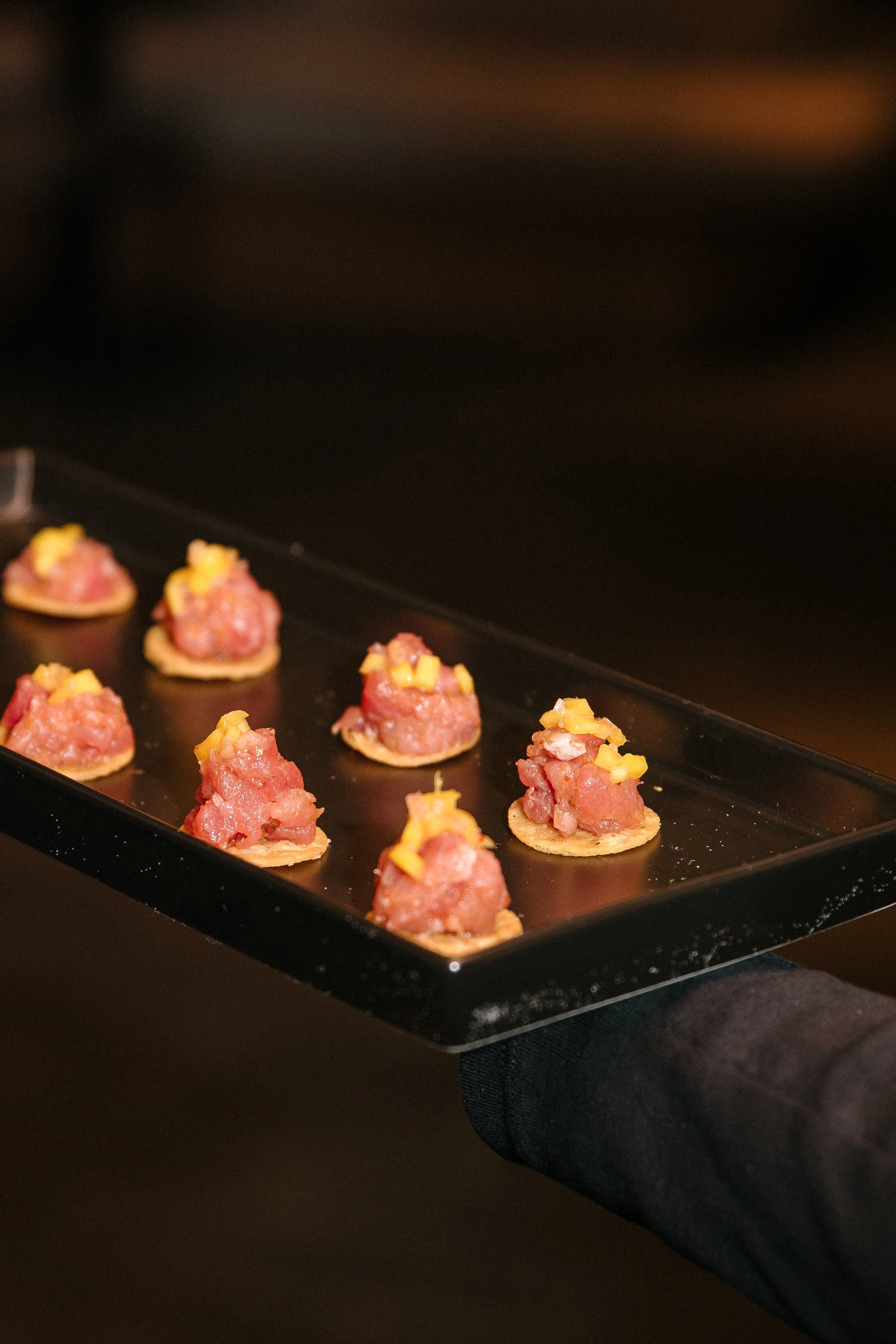 Tray of raw bite-sized appetizers topped with diced yellow and pink ingredients.