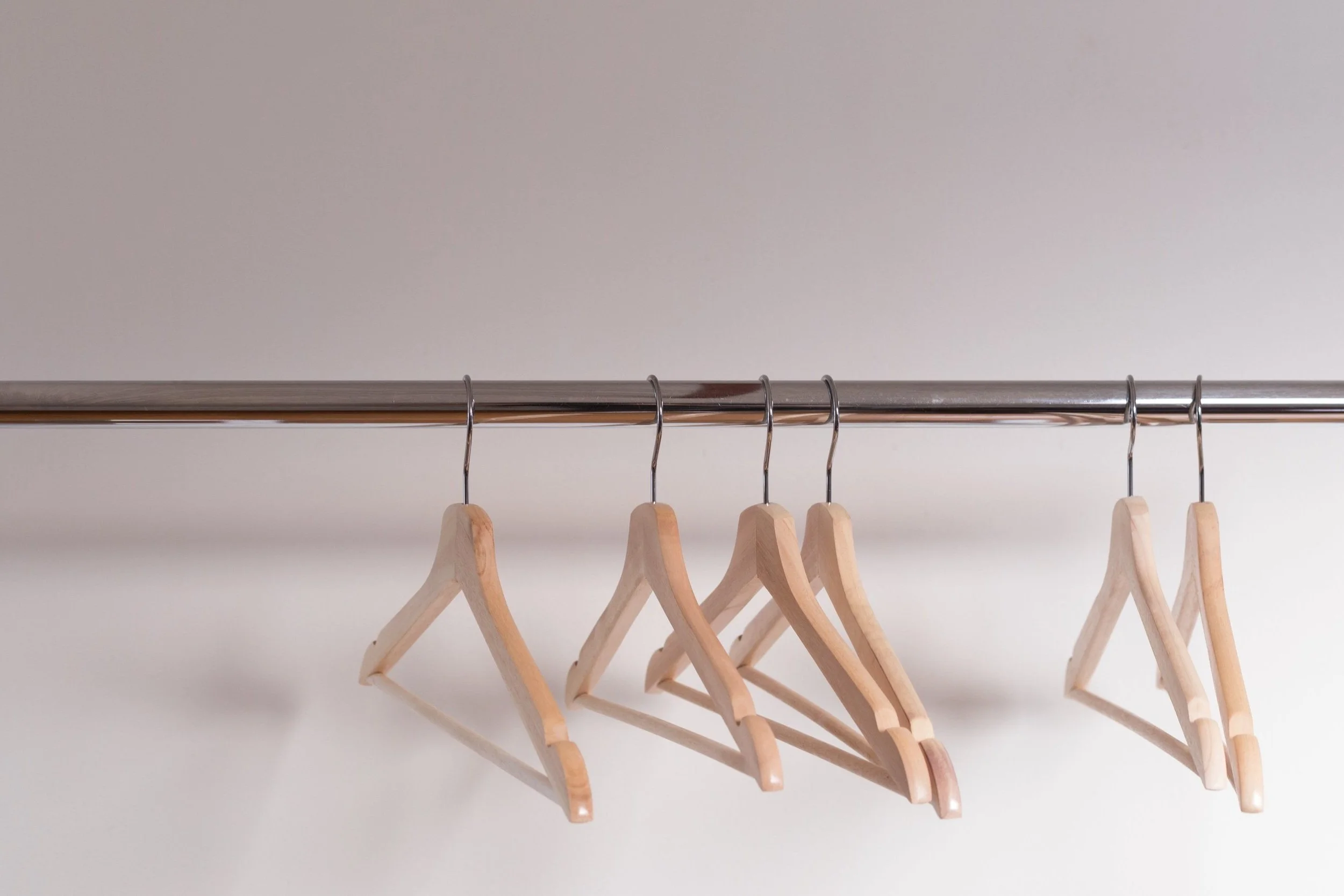 Tan wood clothing hangers on a shiny silver metal clothing rack with a neutral background