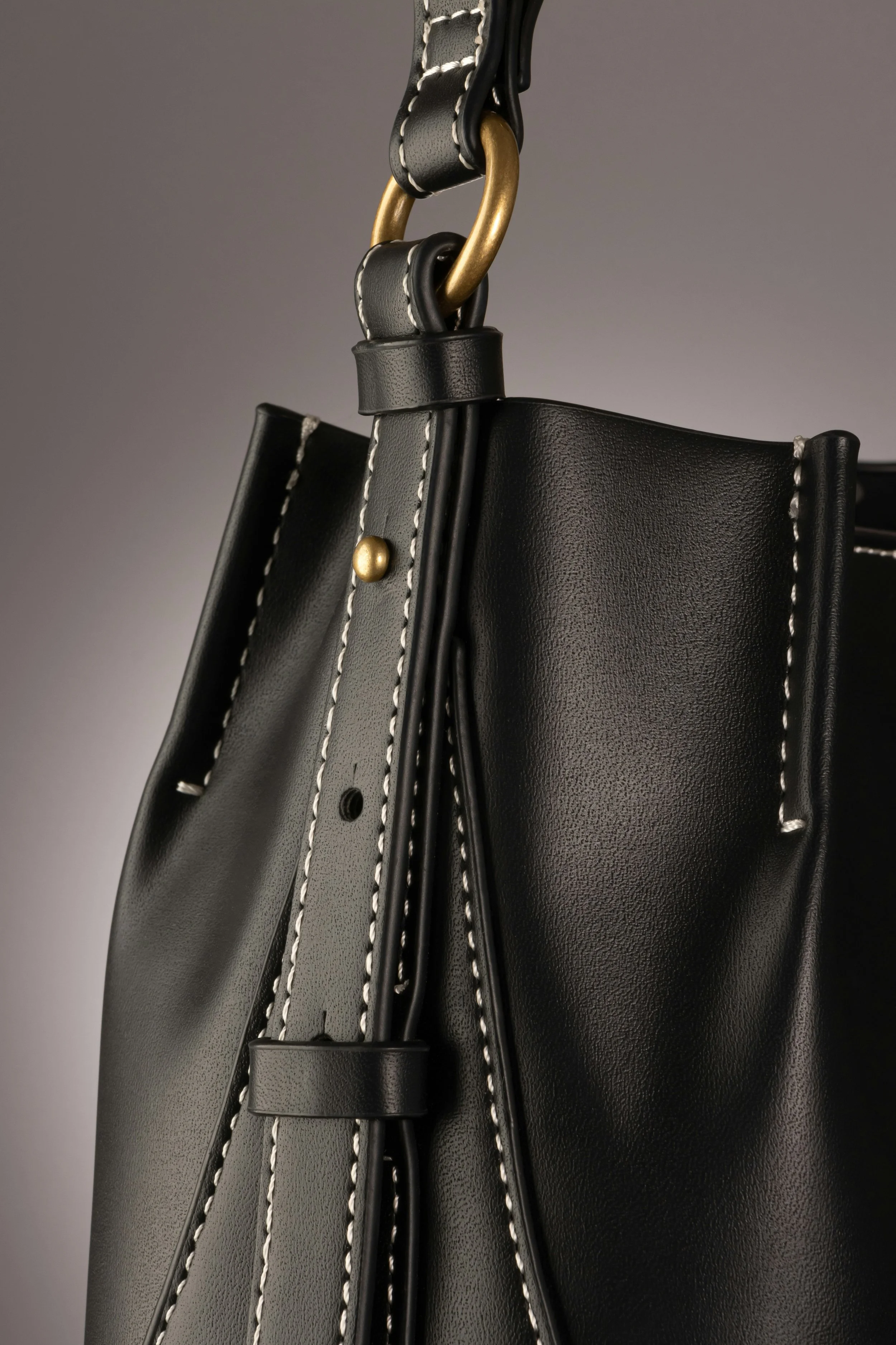 Up close image of a black smooth leather handbag with gold hardware and white contrast stitching on a grey background