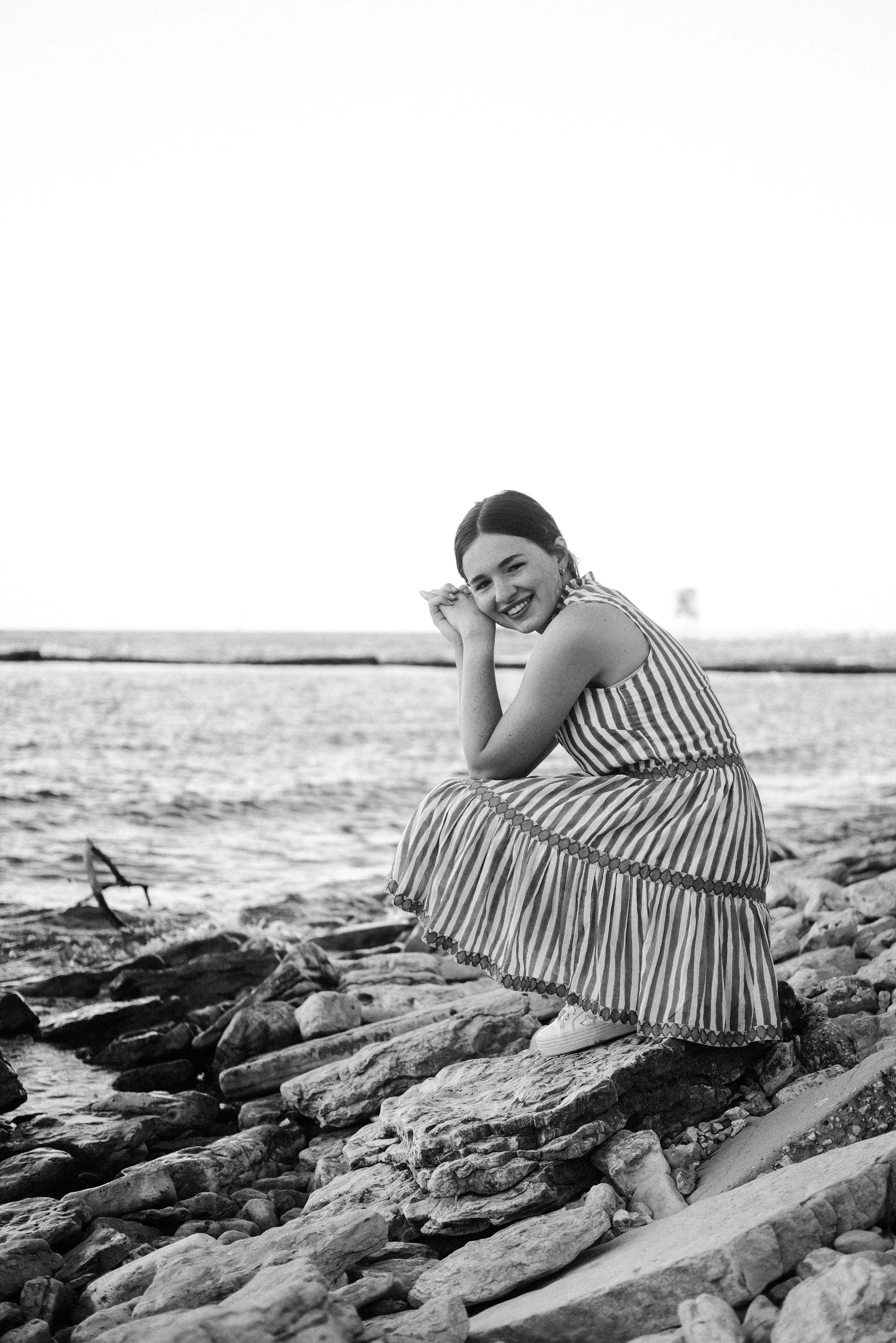 Black and white image of girl crouched down at the lakeshore