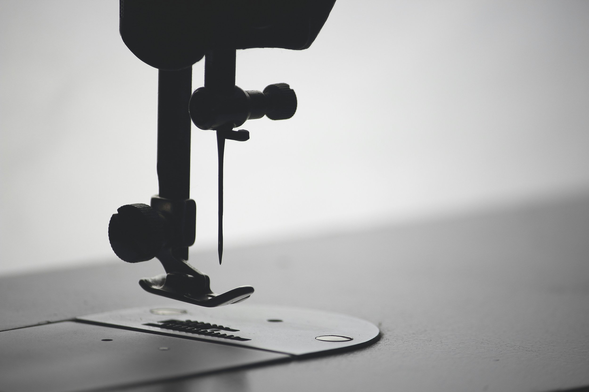 A black and white up close image of a sewing machine, the needle, foot and feed dogs.