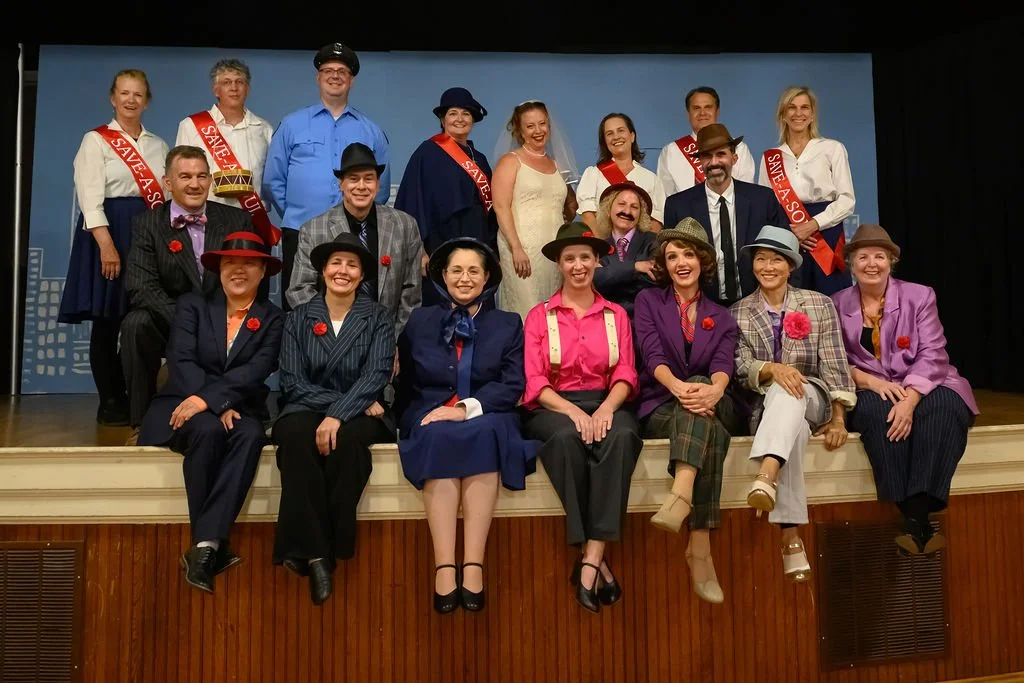 Group of people in vintage costumes on stage, some with 'SAVE A SOUL' sashes, smiling and posing for a photo.