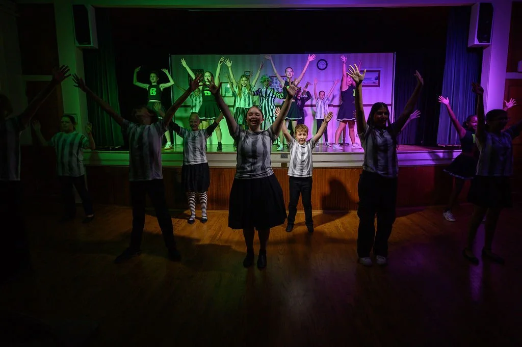 Children dancing on stage with a colorful background, some with arms raised in celebration, in a performance setting.