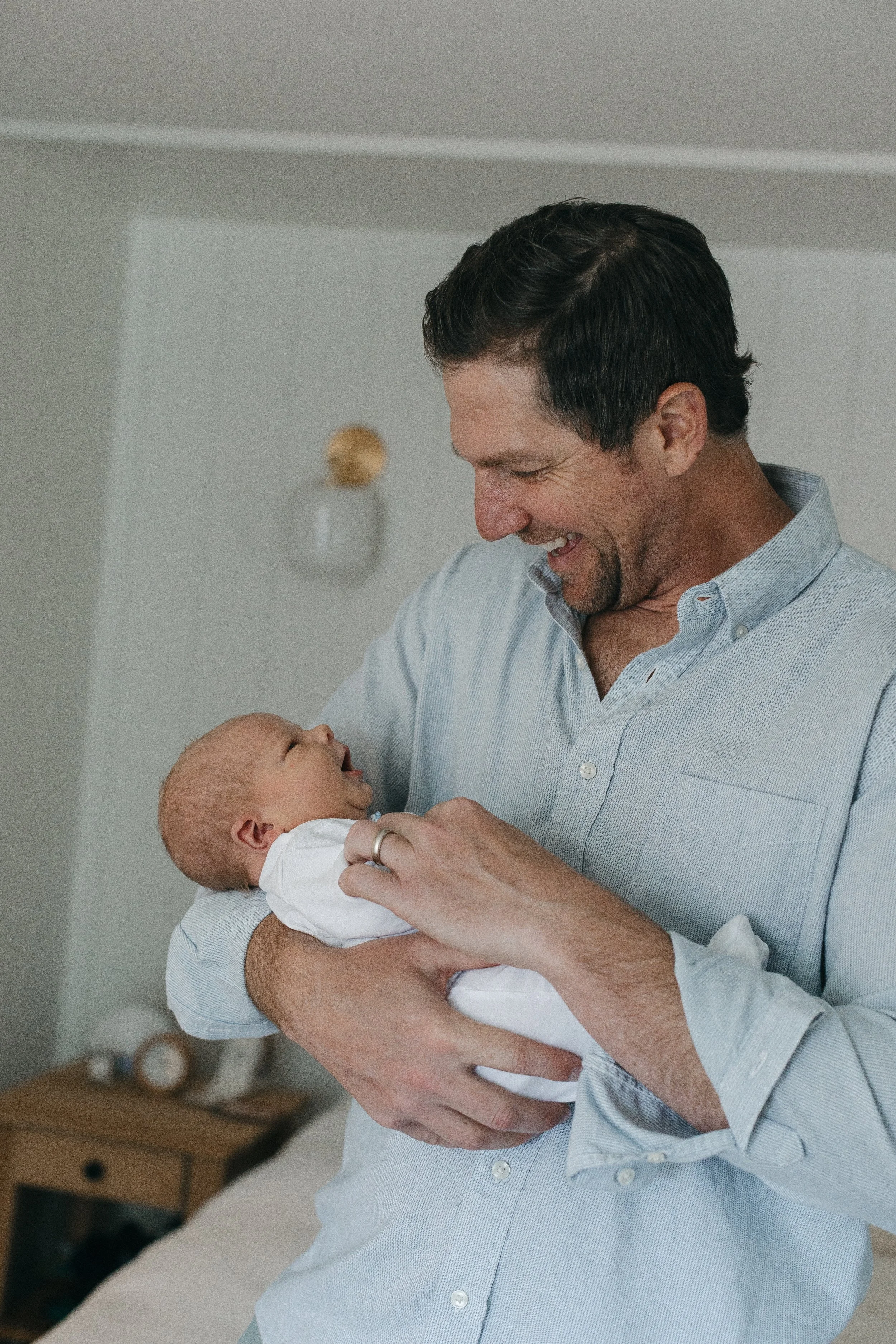 A man holding a baby and smiling warmly in a softly lit room.
