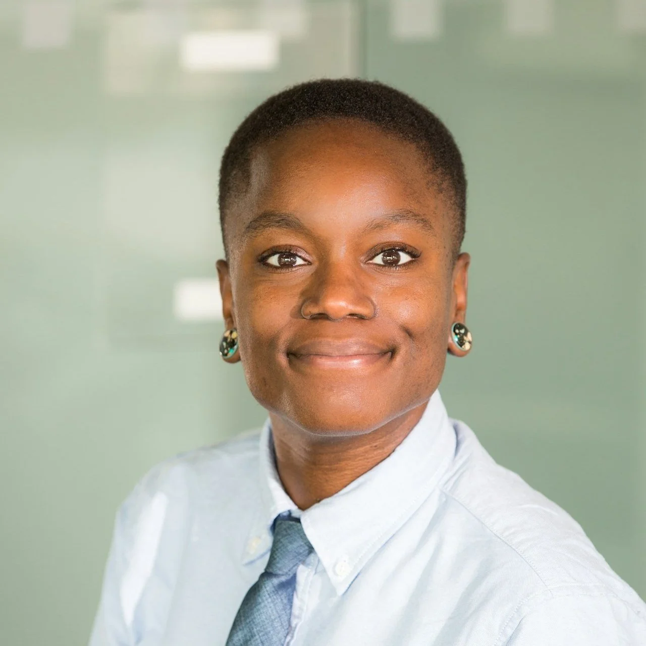 Black woman with short natural hair smiling softly in a button-up shirt, conveying warmth and confidence in a professional setting.