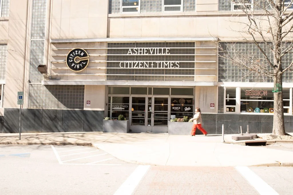 Front view of the Asheville Citizen-Times building with signage, windows, and a person walking on the sidewalk.
