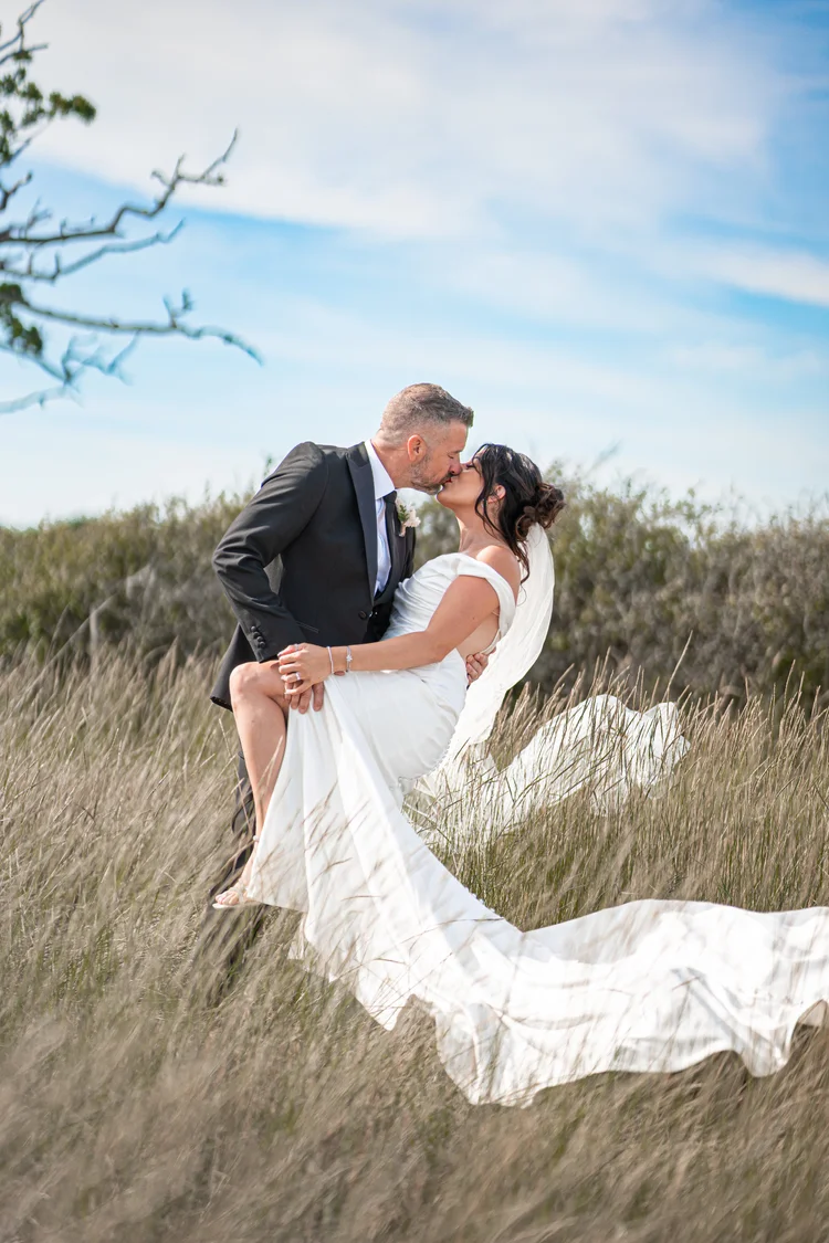 A bride and groom sharing a kiss in a sunlit field on their wedding day