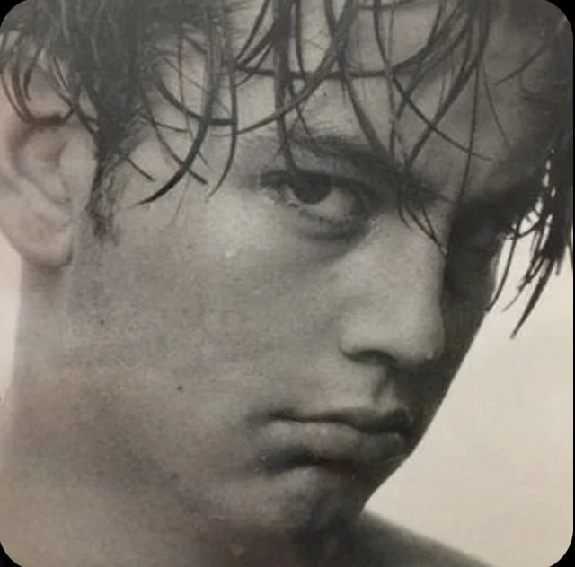 Close-up black and white photo of a young man with messy hair, intense gaze, and full lips.