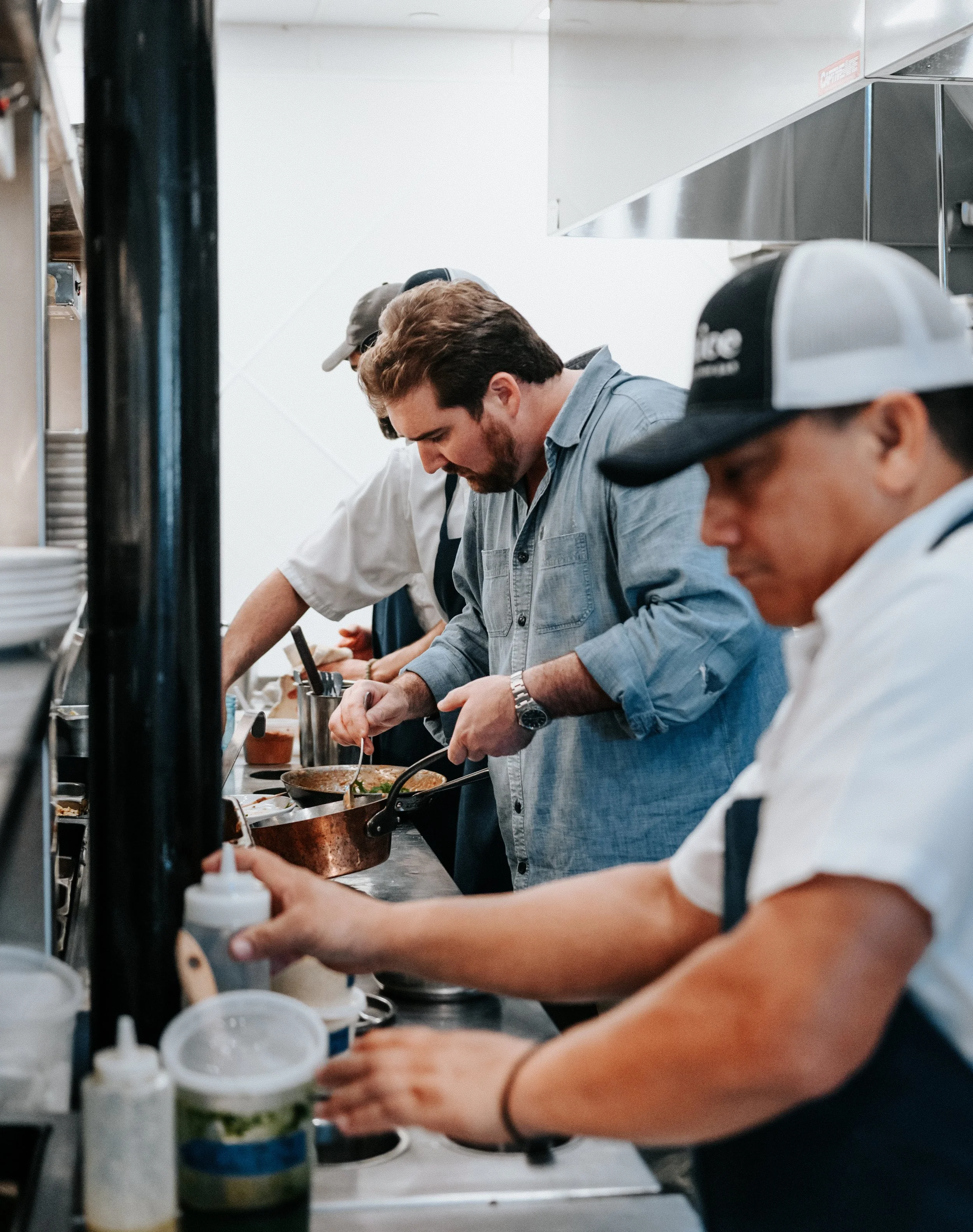 People working in a commercial kitchen, cooking and preparing food on a countertop.