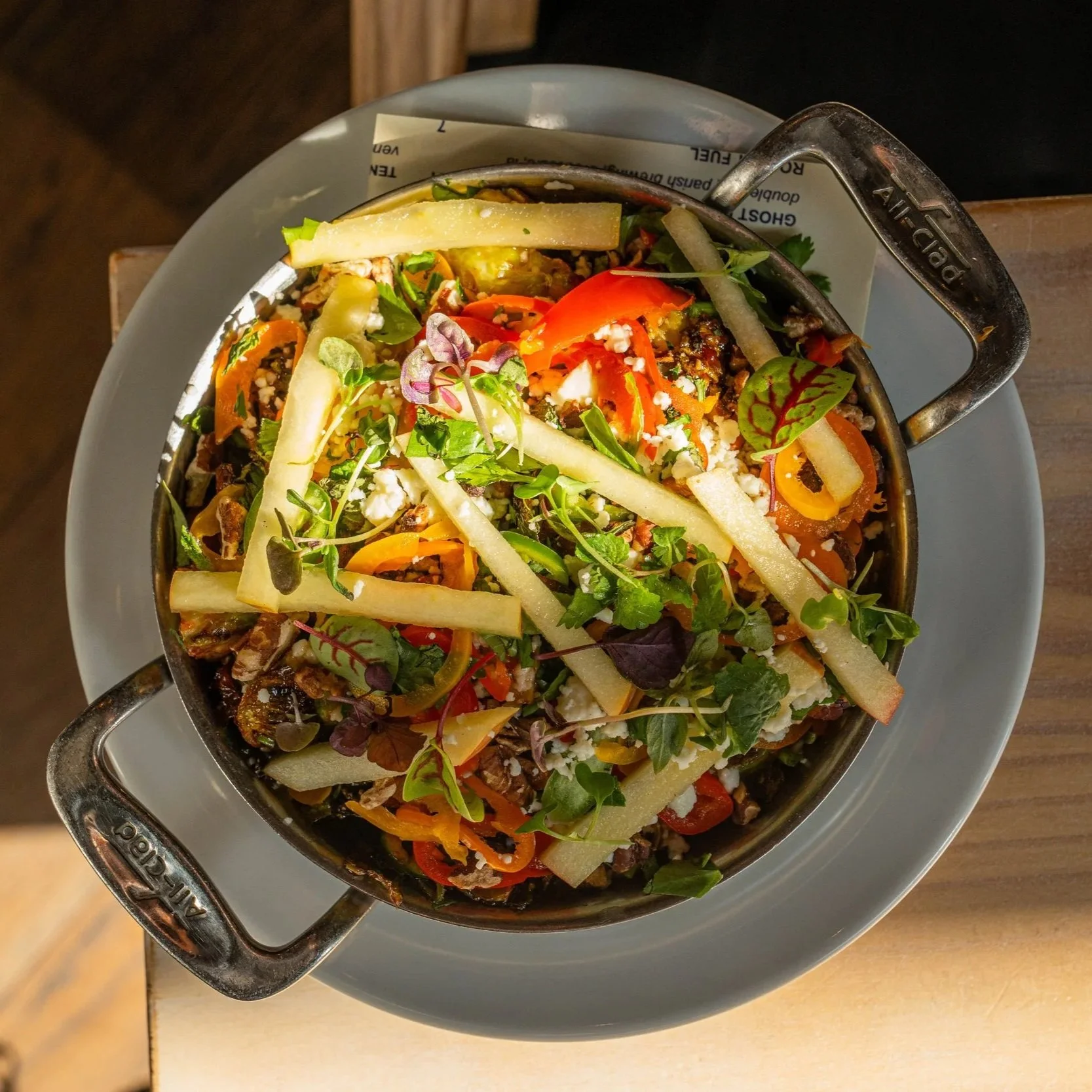 Colorful salad with vegetables and crumbled cheese in a small metal dish on a white plate.
