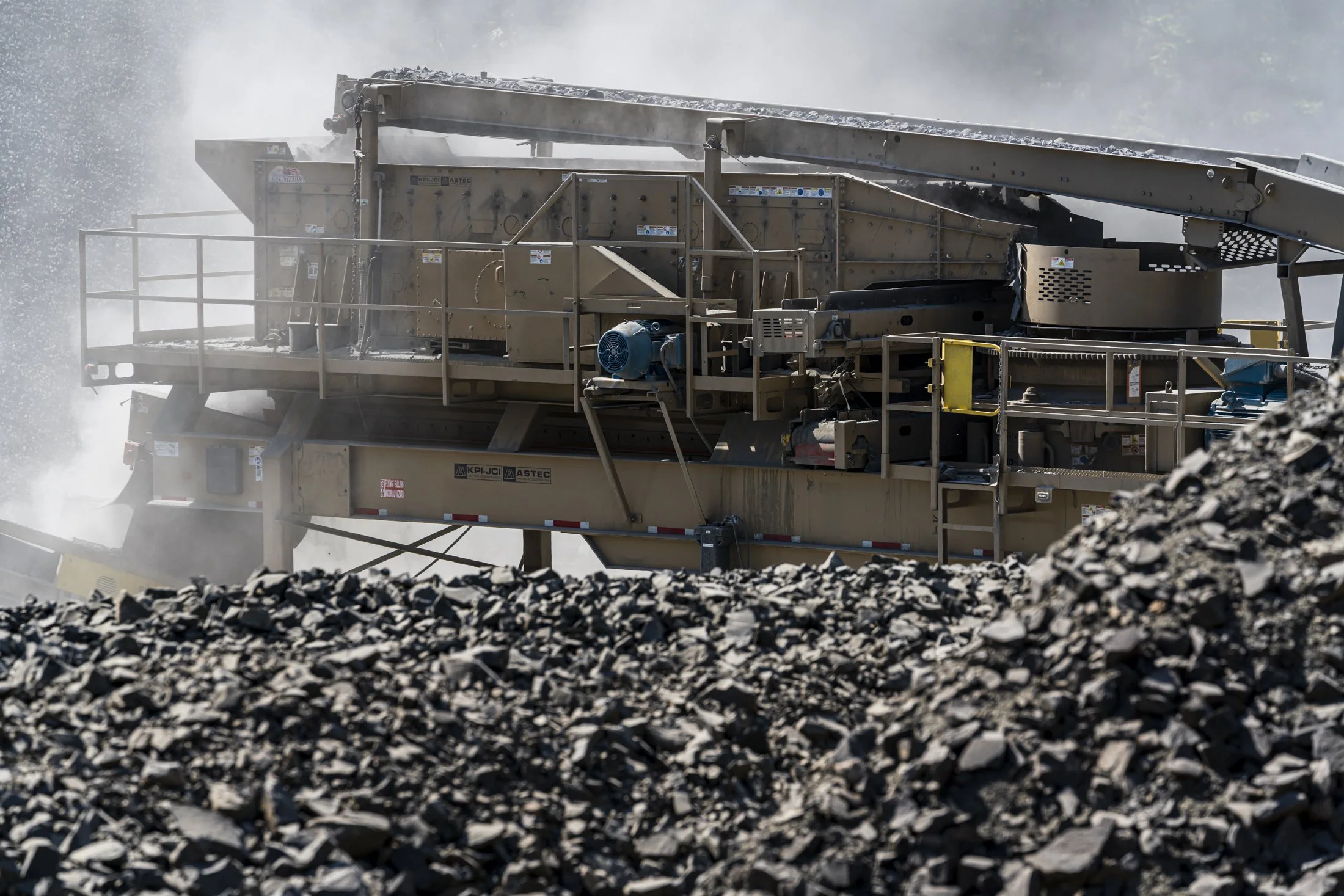 A large industrial mining machine crushing rocks in a quarry, with dust and debris flying around.