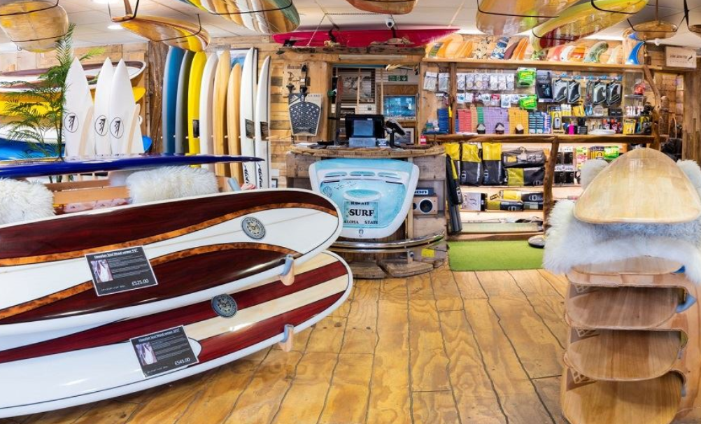 Interior of a surf shop with surfboards displayed, shelves with accessories, and a checkout counter.