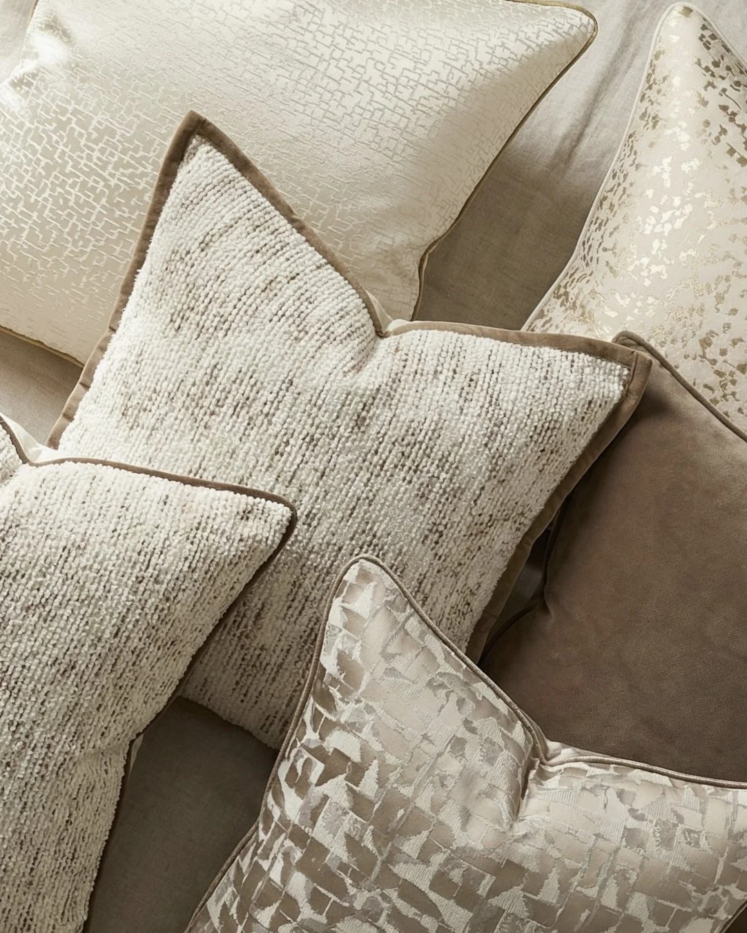 A collection of decorative pillows in cream, beige, and taupe tones with various textures and patterns on an upholstered sofa.