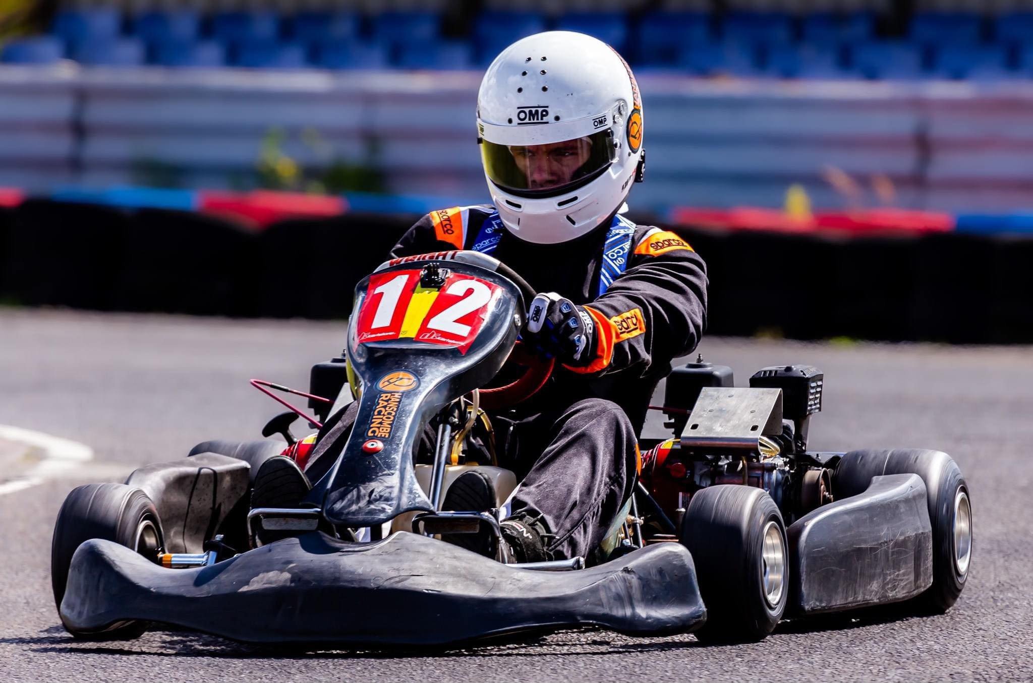 Person driving a go-kart with a racing helmet and suit on a track.