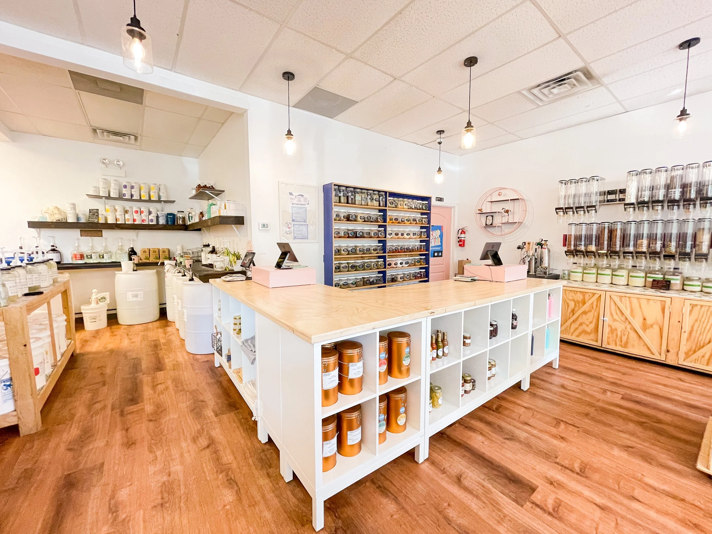 Interior of a bulk store with wood floors, white walls and shelves with dispensers.