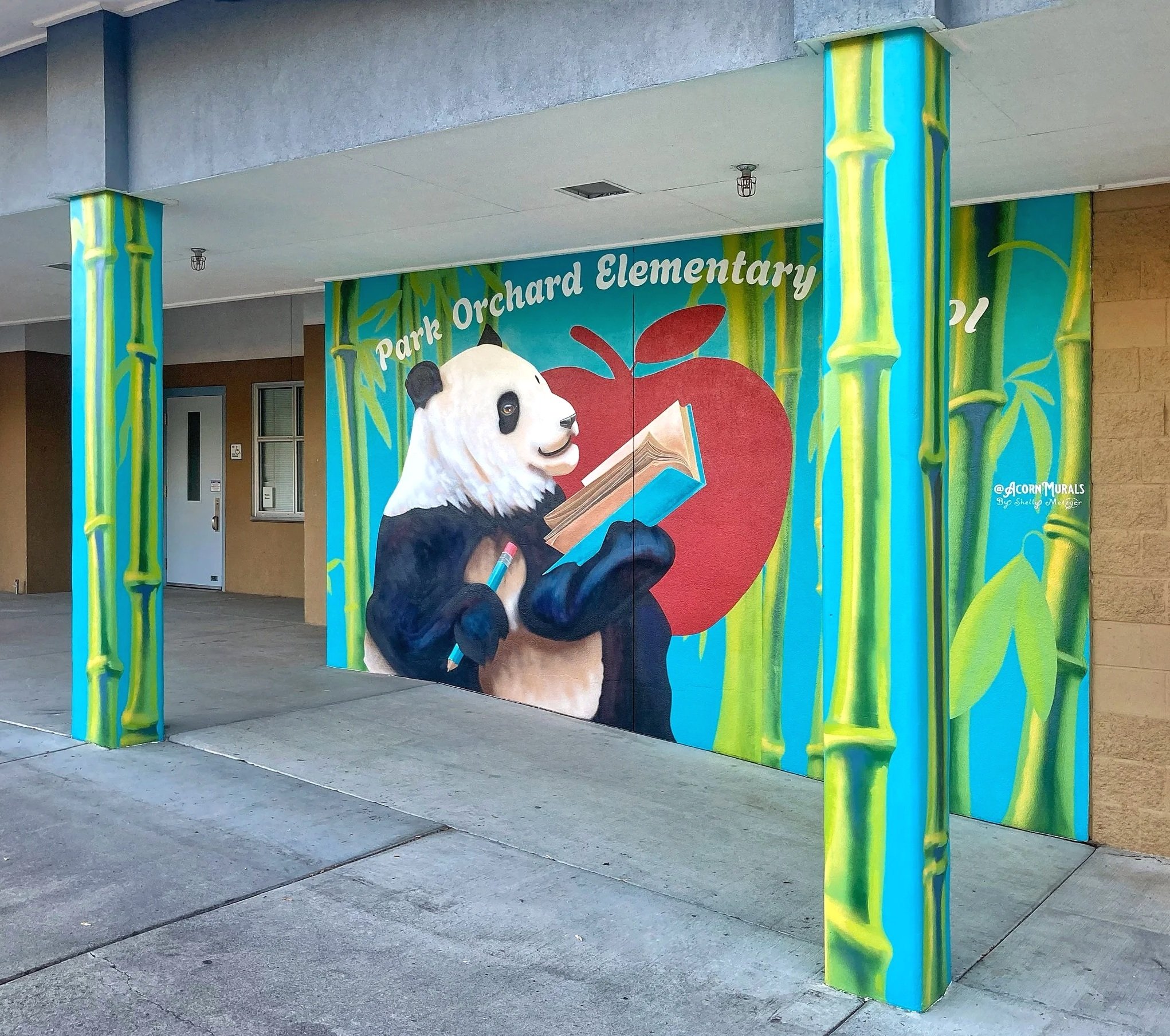 Acorn Murals Shelly Metzger Hungry for Knowledge Panda mural for Park Orchard Elementary School Kent, WA Panda holding a book and pencil over an apple symbol, surrounded by a bamboo forest. Angle highlights mural wraps around surrounding pillars. 
