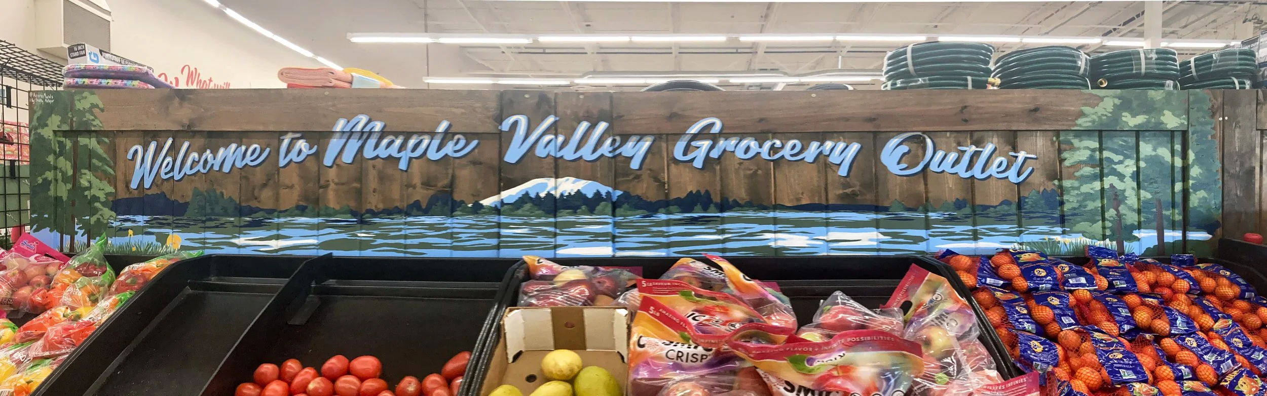 Mural Sign Painted for Maple Valley Grocery Outlet, features a rustic wooden back drop, and national park like design. Inspired by Lake Wilderness, and Mount Rainier, welcoming customers into the store. Custom Mural for Grocery Store Hand Painted, an