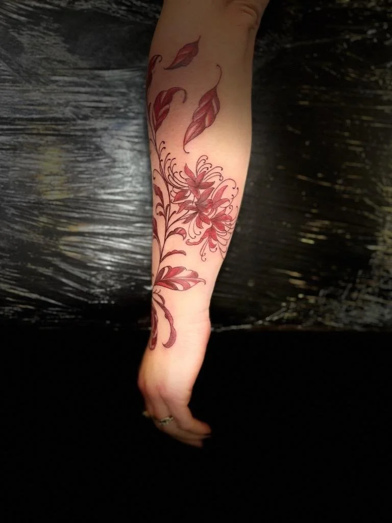 Tattoo of red and pink flowers and leaves on a person's forearm.