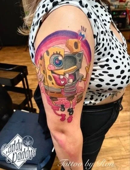 Tattoo of SpongeBob SquarePants holding a camera on a person's upper arm.