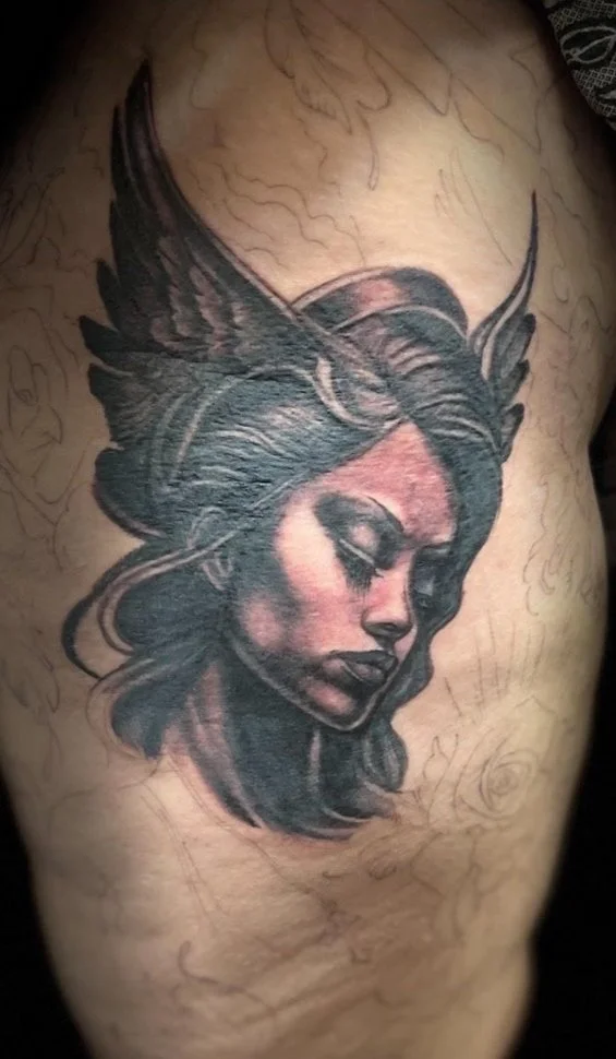 Tattoo of a woman's face with closed eyes, dark hair, and a headdress resembling horns or wings, on a person's ribcage.