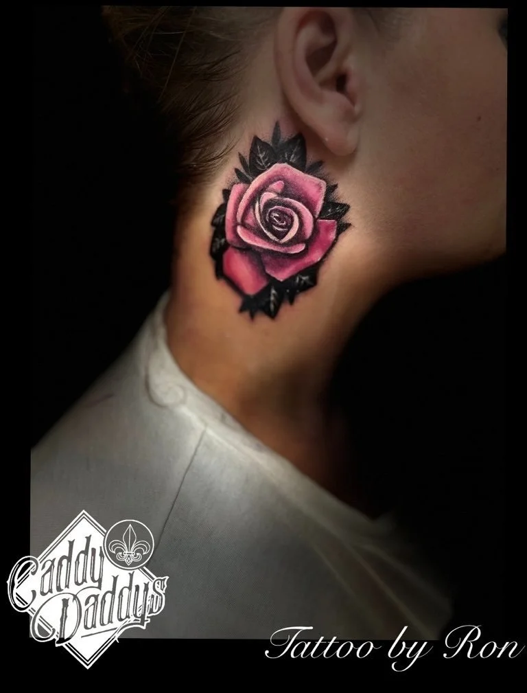 Close-up of a woman's neck and ear showing a pink and black rose tattoo behind her ear.