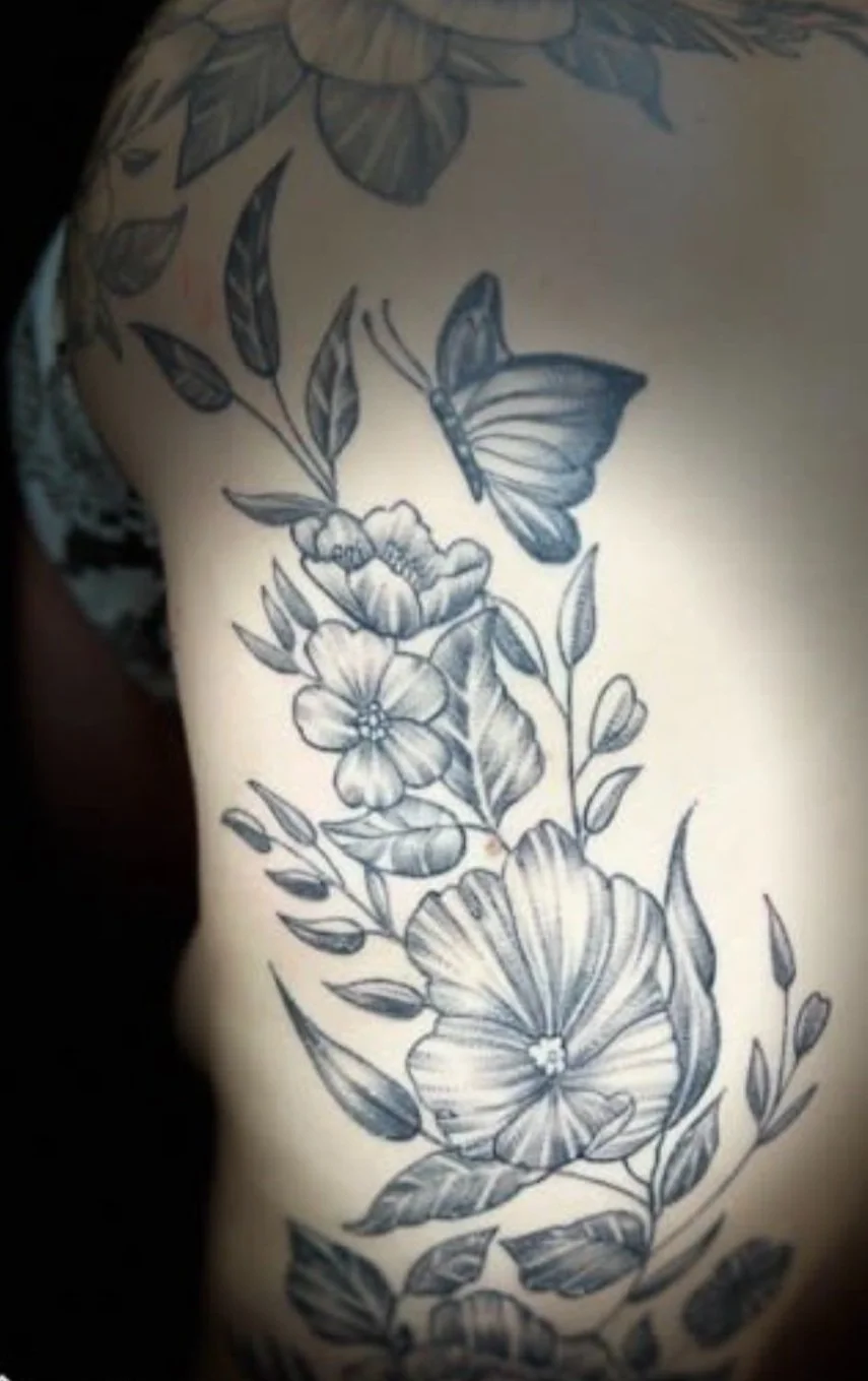 Black and gray tattoo of butterflies, flowers, and leaves on a person's upper arm.