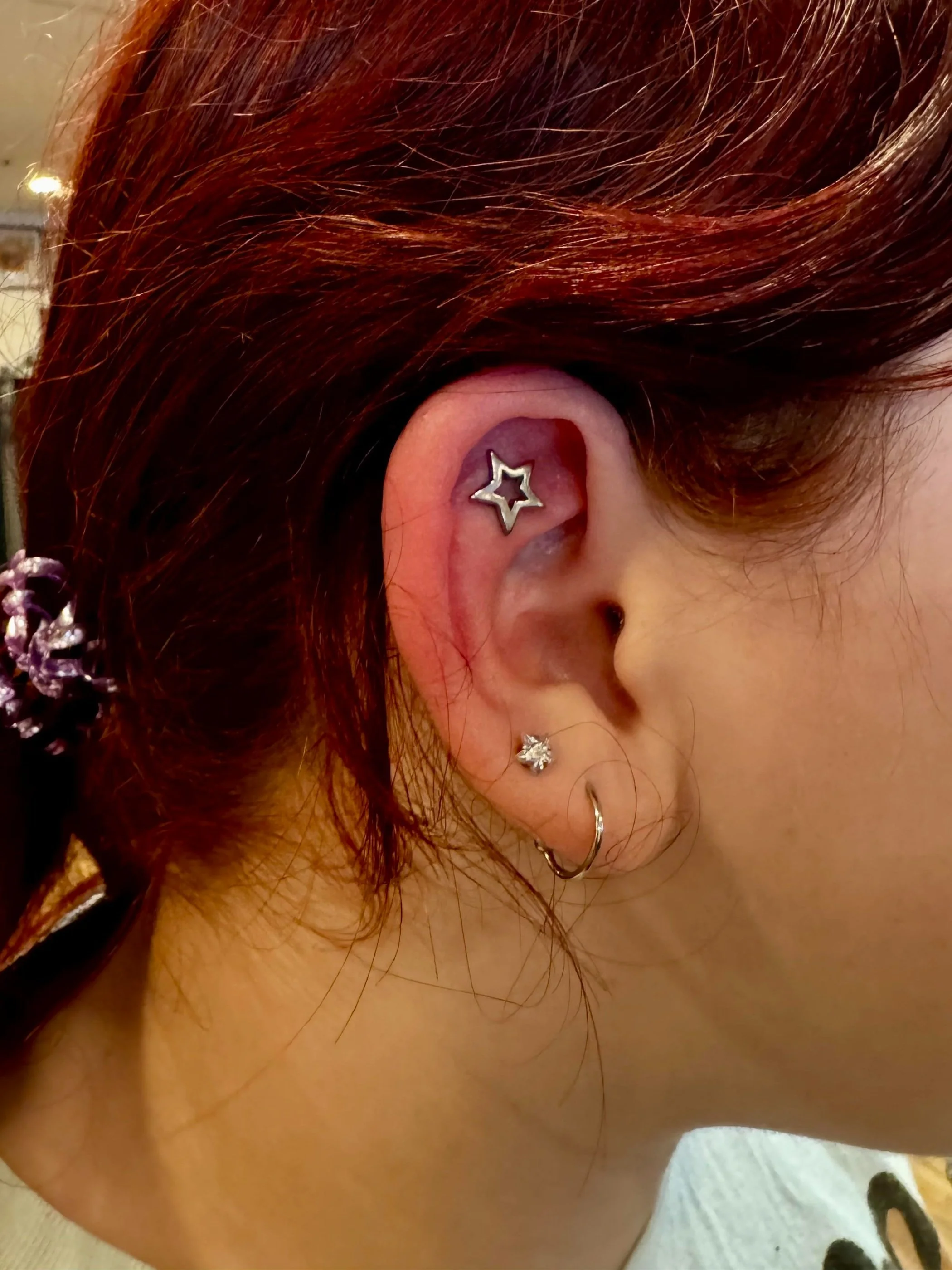 Close-up of a person's ear with four piercings, including a star-shaped cartilage earring, a small flower-shaped earring, and a hoop earring which were just pierced at Caddy Daddy's