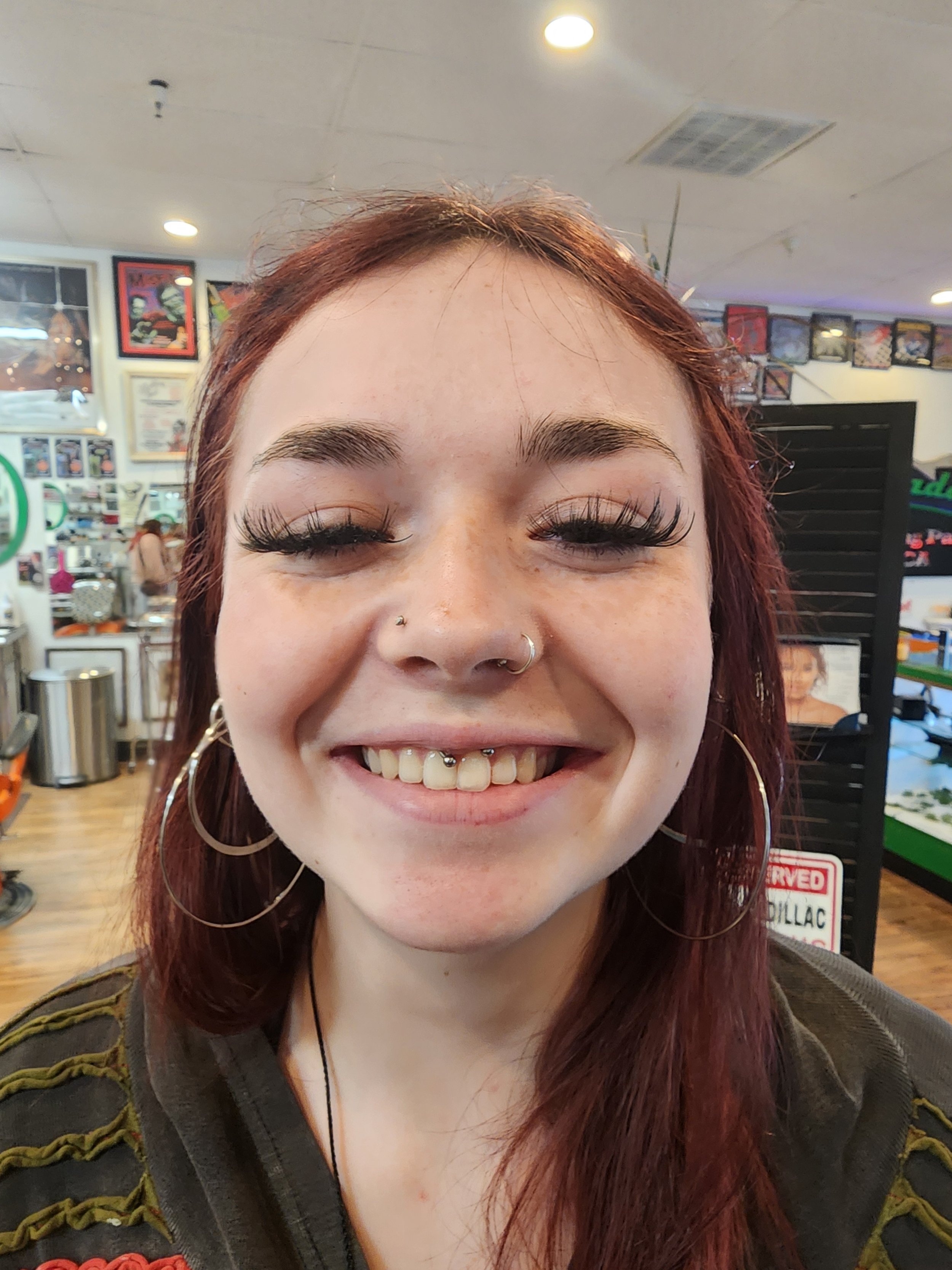 Close-up of a young woman smiling with closed eyes, wearing large hoop earrings, a nose ring from professional piercing store in Redding
