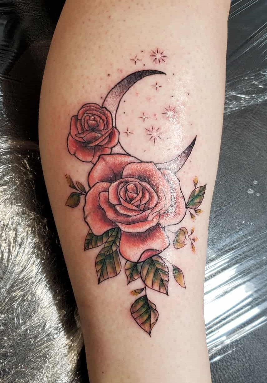 Tattoo of two roses with leaves, a crescent moon, and stars on a person's arm.