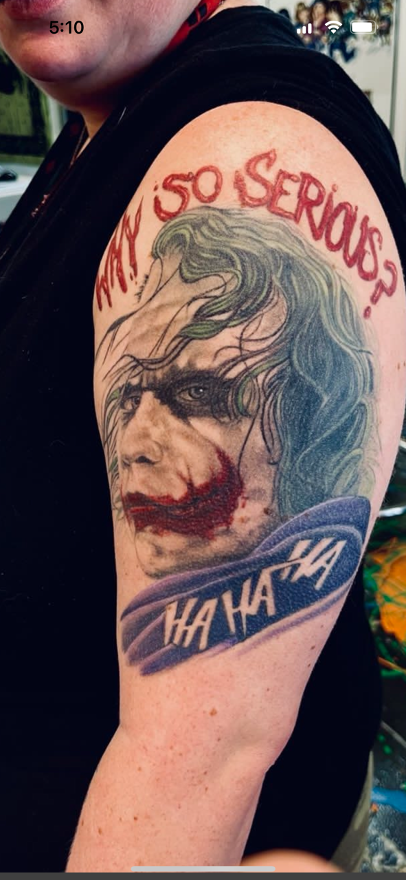 Tattoo of the Joker with red text above reading 'WHY SO SERIOUS?' and laughing text below reading 'HAHAHA'.