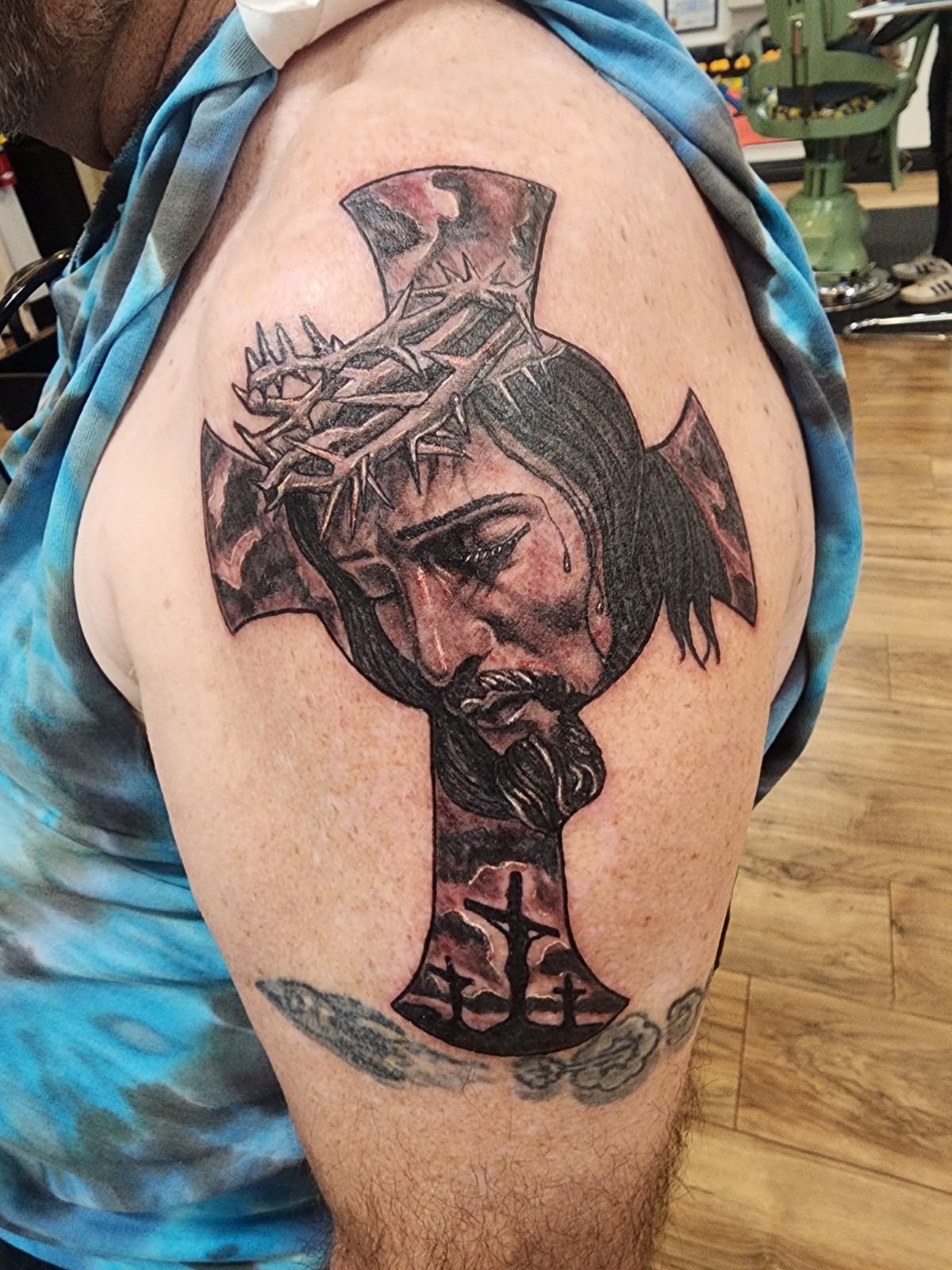 Woman with a tattoo of a crown of thorns, Jesus Christ, with dark hair and tears on her face, surrounded by a red and black cross shape from a Redding tattoo artist
