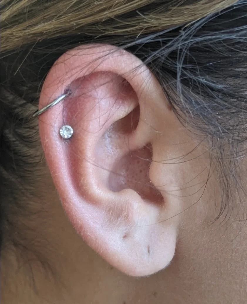 Close-up of a human ear with a diamond stud earring in the lower piercing and a curved barbell in the upper piercing from a piercing shop in Redding CA