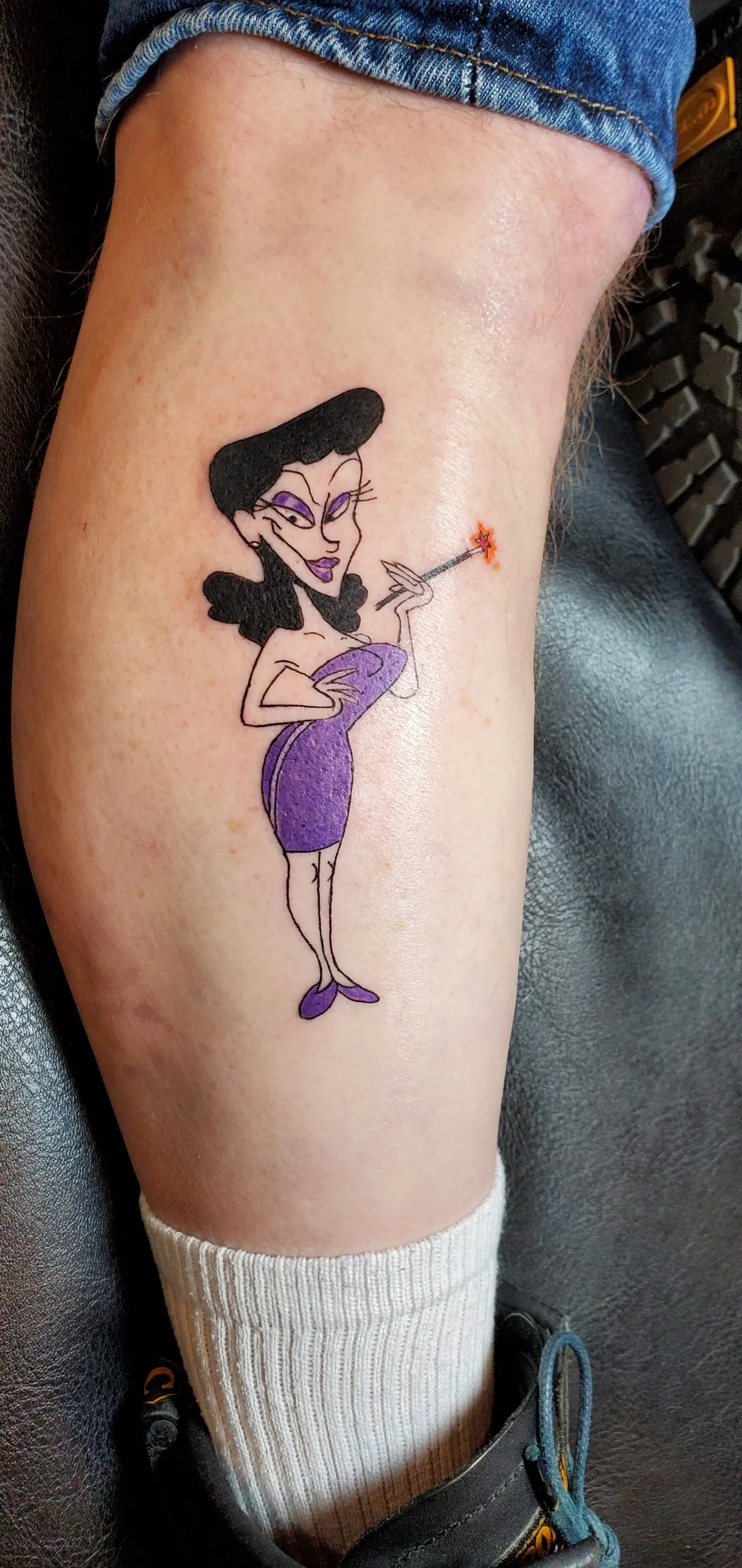 Tattoo of a cartoon woman with black hair in a purple dress holding a magic wand with a star on the tip, standing on a person's leg.