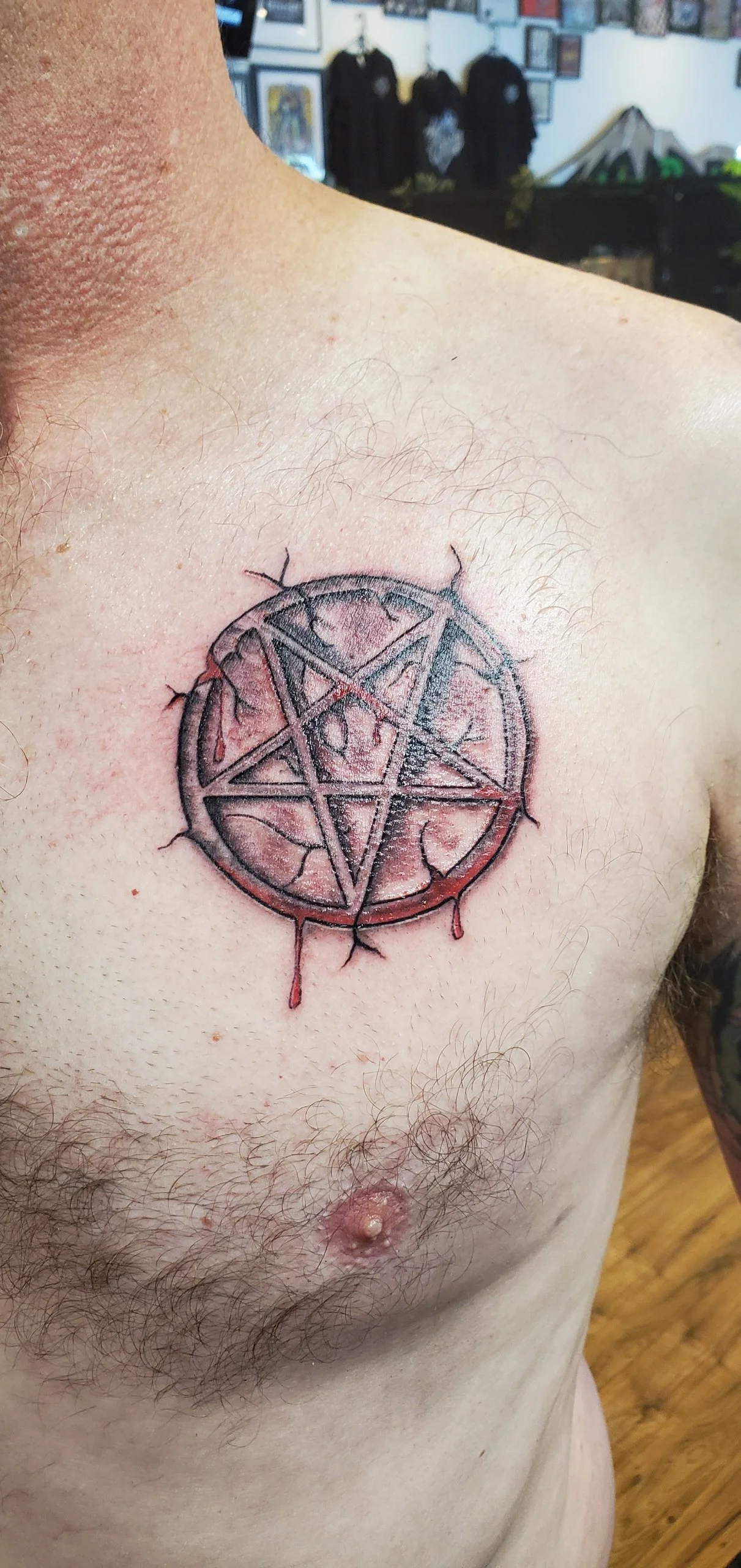 A tattoo of a pentagram inside a circle with uneven edges and dripping effect, on a person's chest.