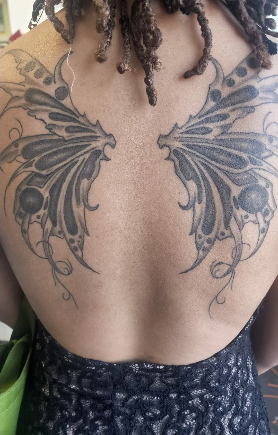 A monochromatic tattoo of butterfly wings on a woman's back from a professional tattoo shop in Redding