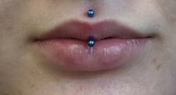 Close-up of a person's lips with a blue labret piercing.
