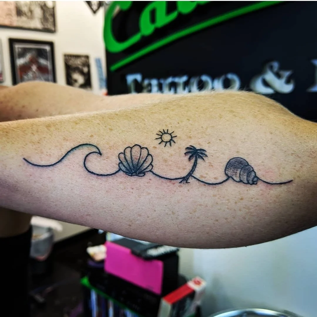Line art tattoo on a person's arm featuring a sun, a seashell, a palm tree, and a conch shell connected by a continuous wavy line from local tattoo artists