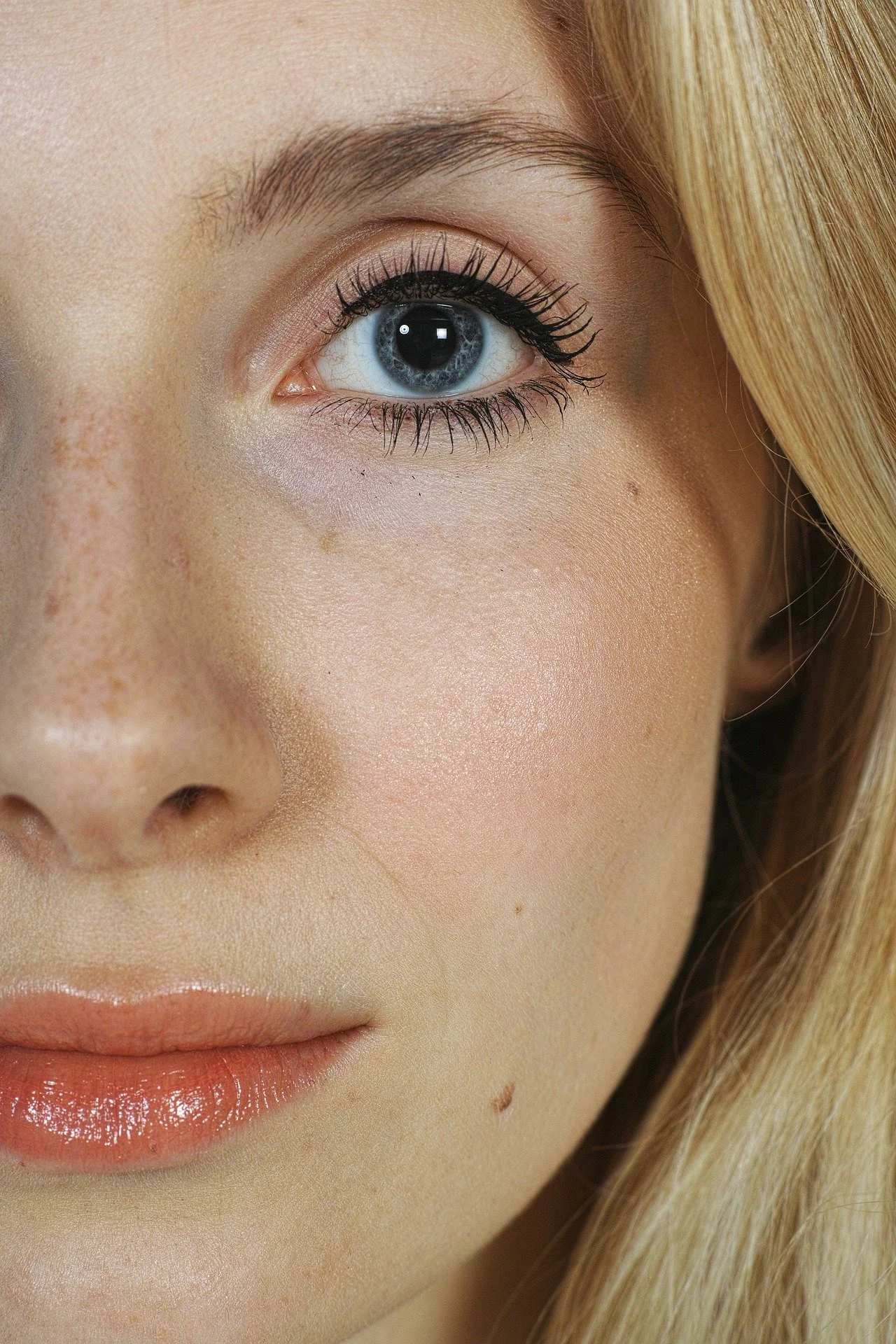 Close-up of a woman's face focusing on her right eye with blue iris, makeup, and blonde hair.